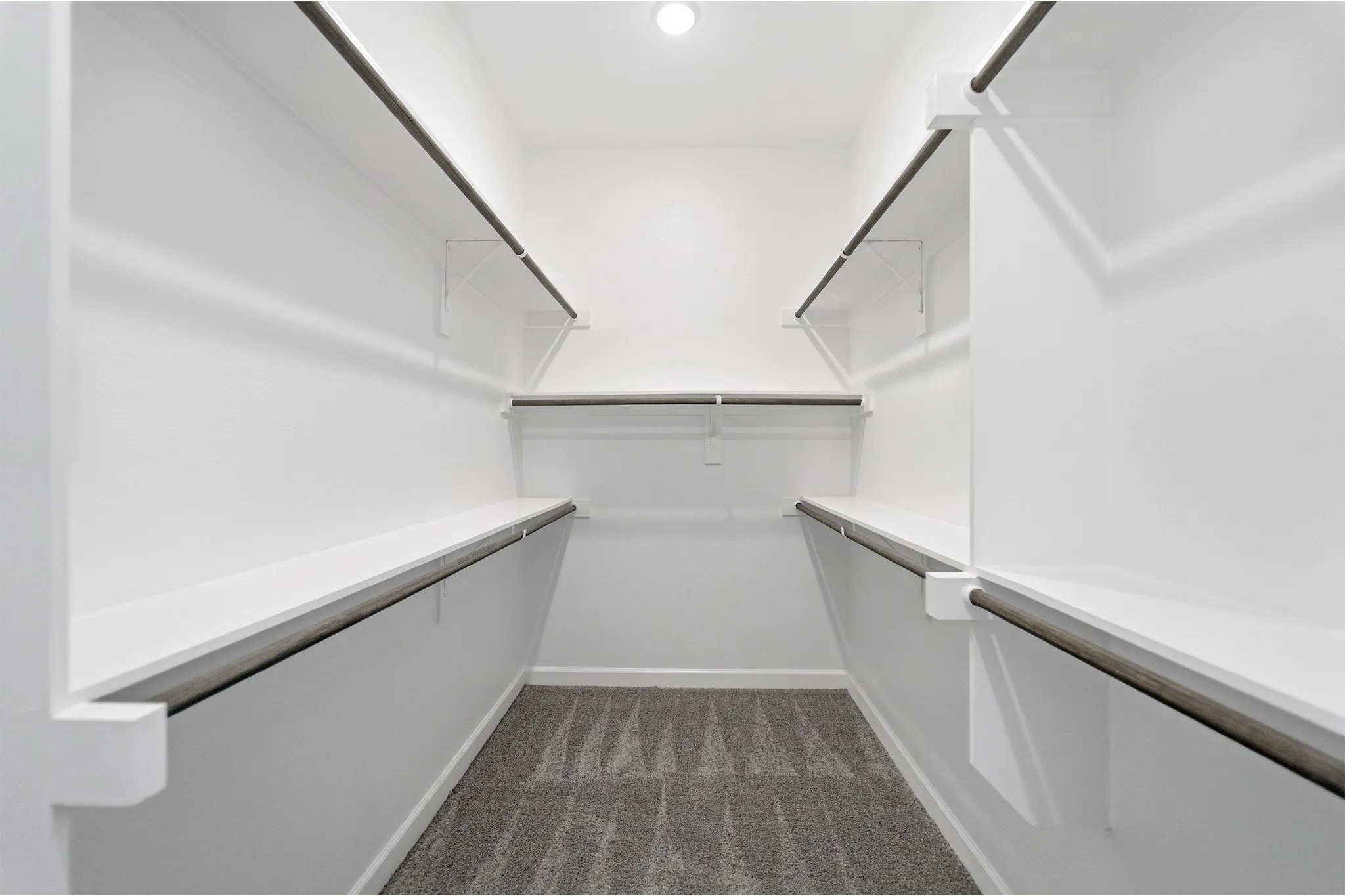 Walk-in closet featuring white shelving and hanging rods, ceiling-mounted light fixture, and patterned gray carpet