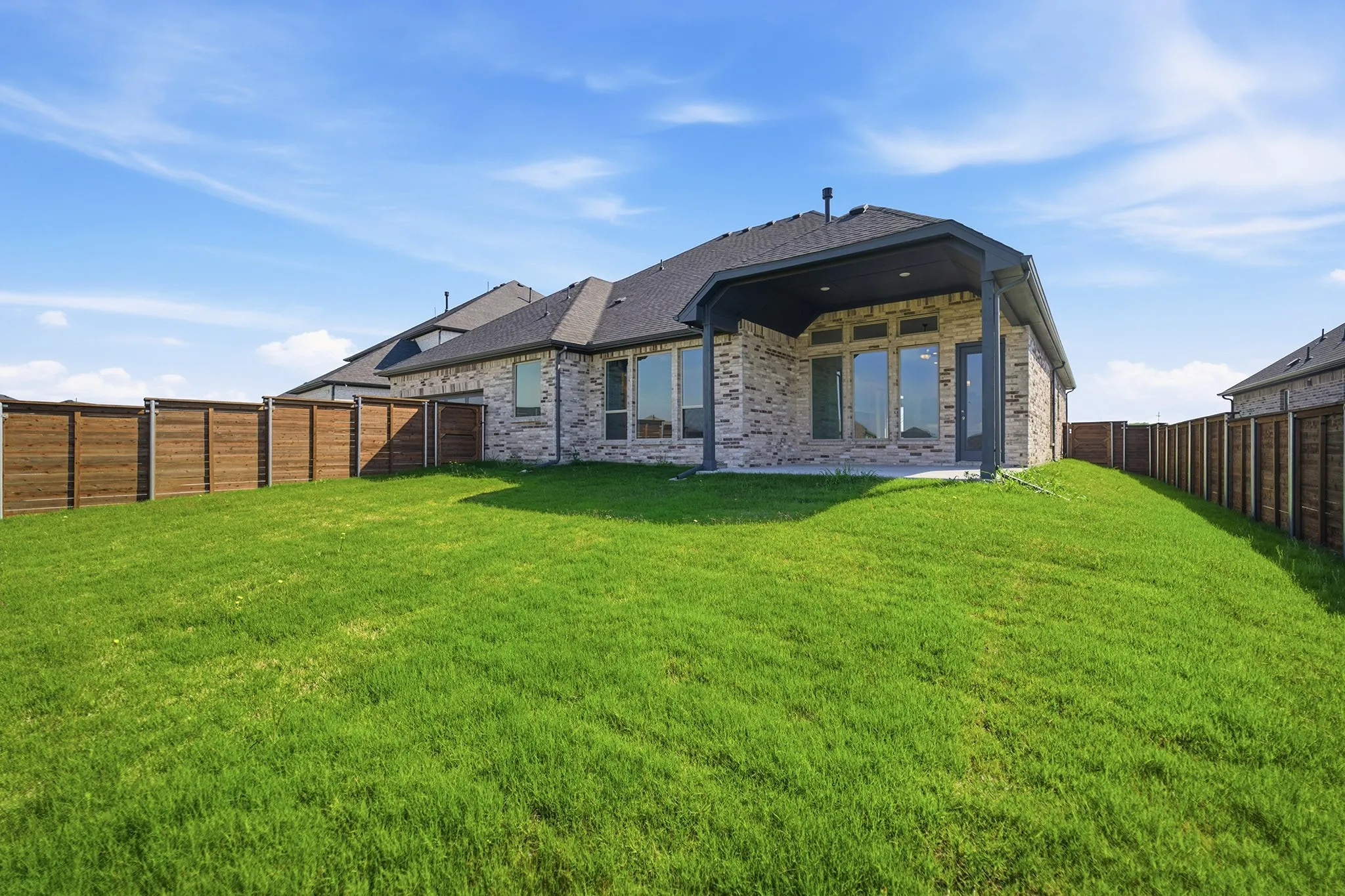 Expansive backyard featuring a lush lawn, privacy fencing, and a covered patio