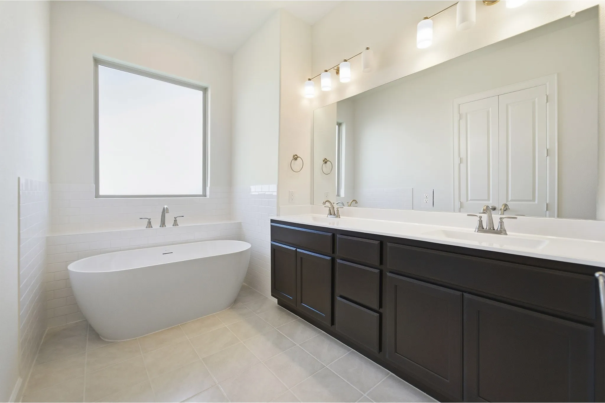 Freestanding soaking tub with brushed nickel fixtures, complemented by a dual vanity featuring dark wood cabinetry and white countertops