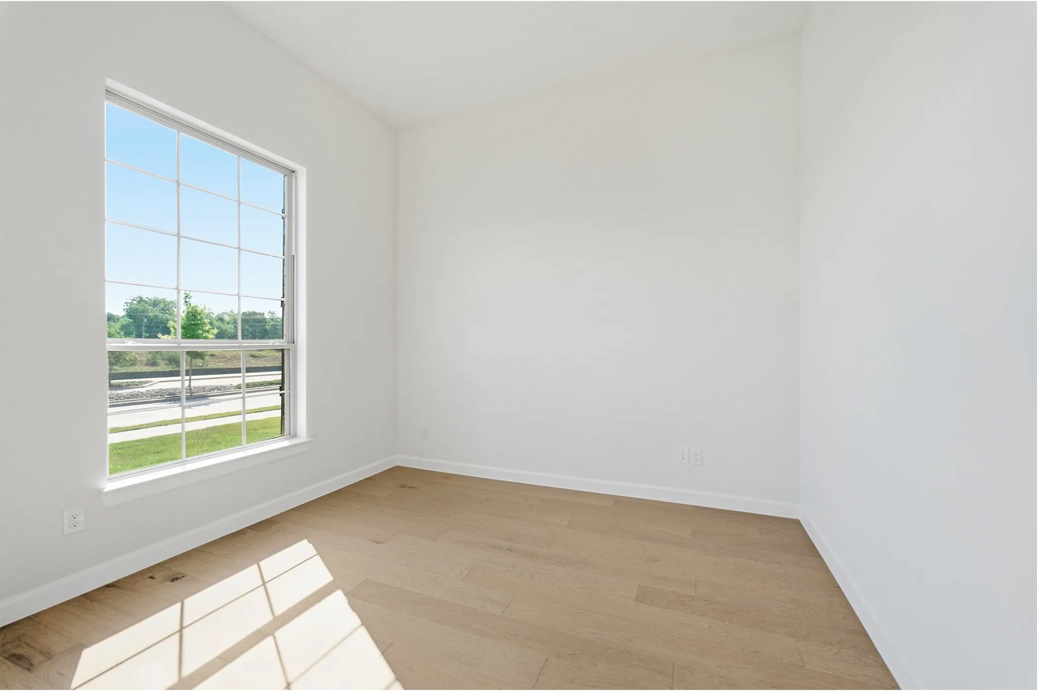 Bright interior space featuring a large grid-pattern window, light wood-finish flooring, and white baseboards