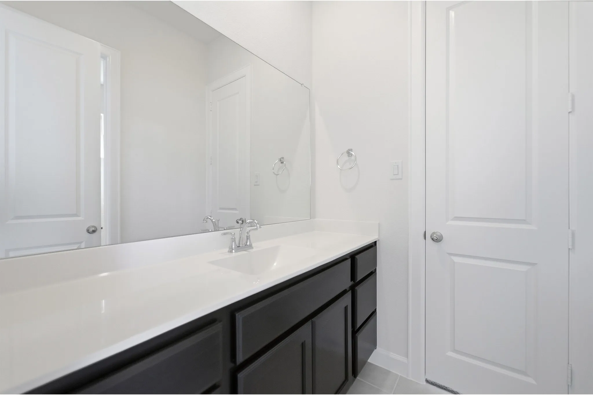 Bathroom featuring a wide vanity with a white countertop, dark wood-finish cabinetry, an integrated sink with a chrome faucet, a large wall-mounted mirror, and tile flooring