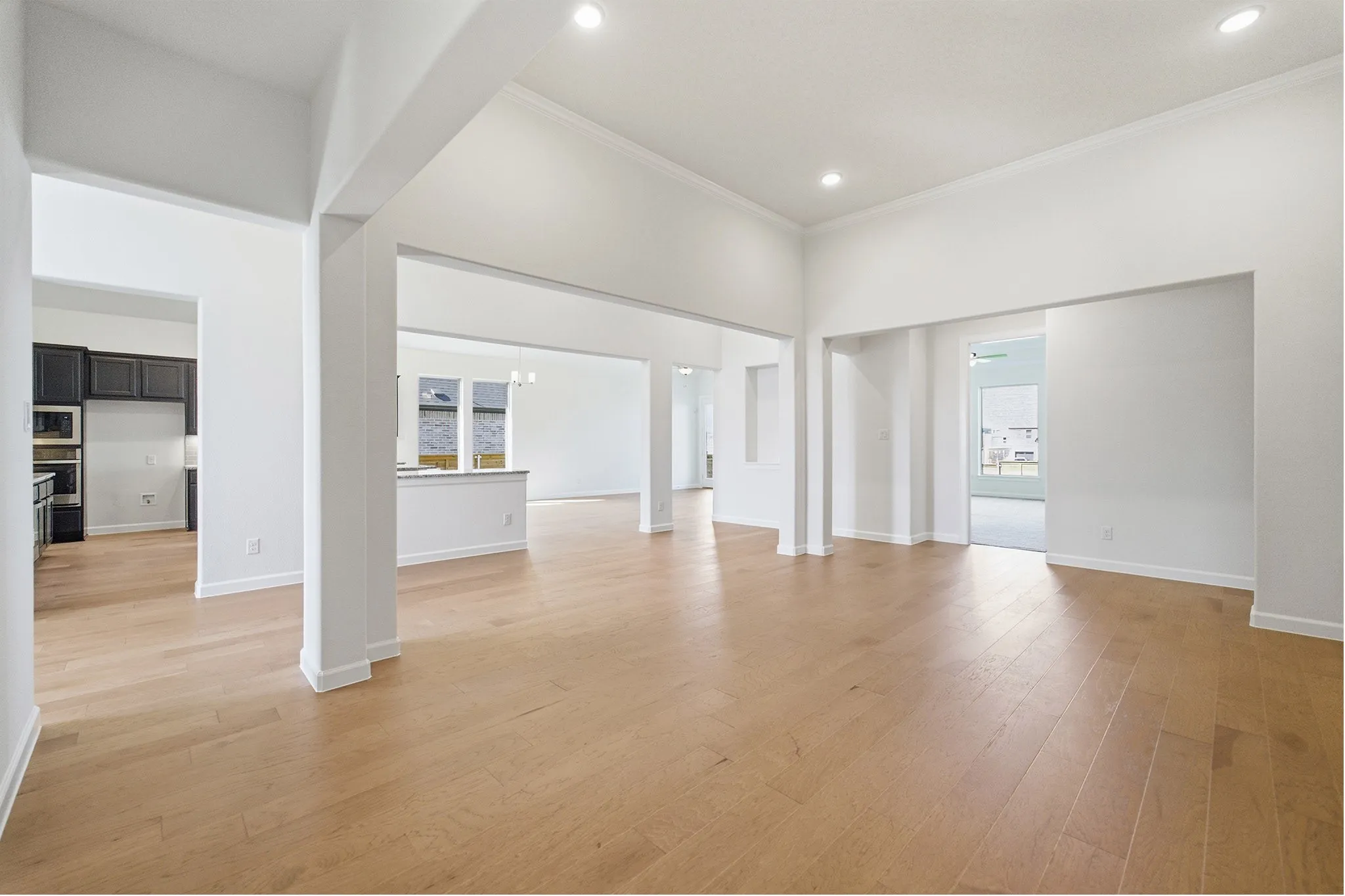 Spacious open-concept living area featuring light wood-finish flooring, recessed lighting, and crisp white walls