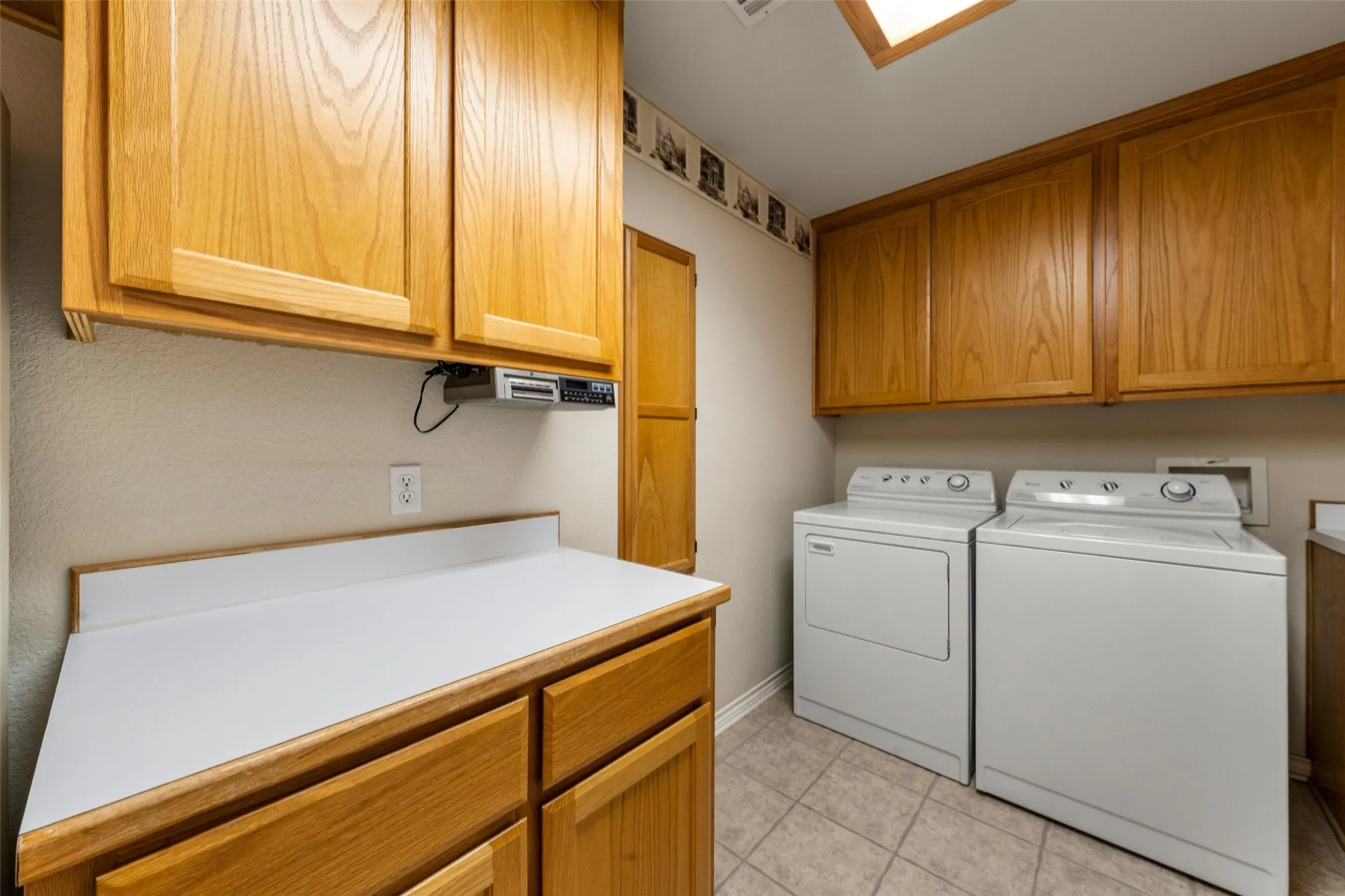Functional laundry room featuring a built-in counter, extensive cabinetry, and neutral tile flooring