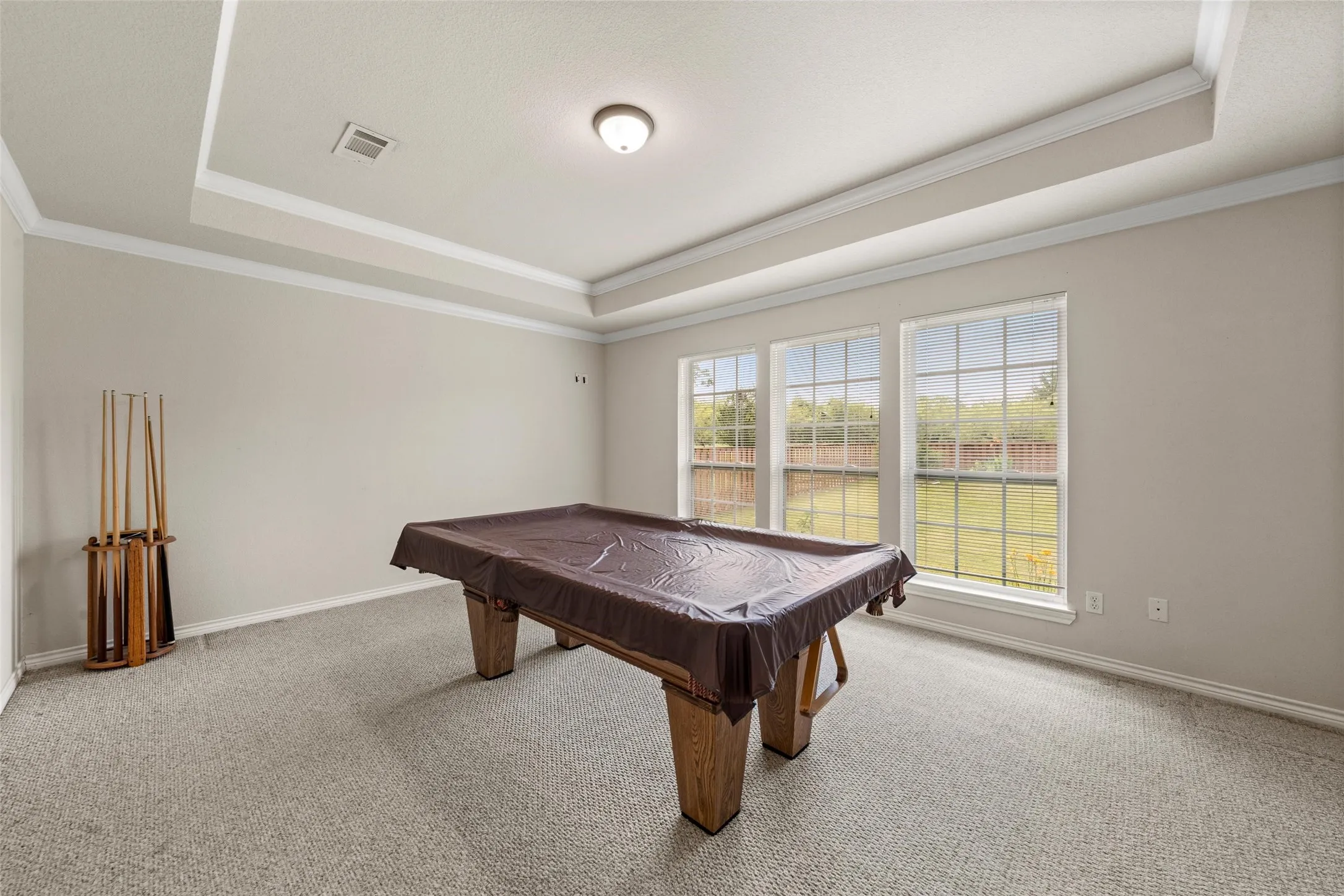 Recessed tray ceiling with crown molding, three large windows, neutral-toned walls, and carpet flooring