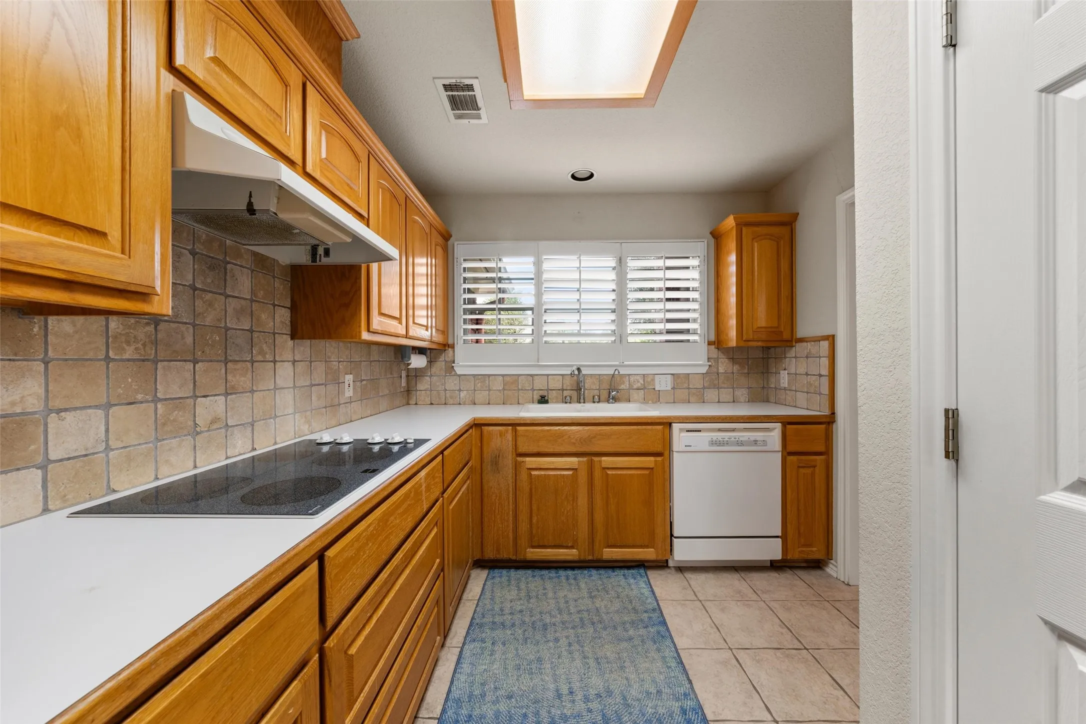 Kitchen featuring wood cabinetry, solid surface countertops, tile flooring, a built-in cooktop, and a matching tile backsplash