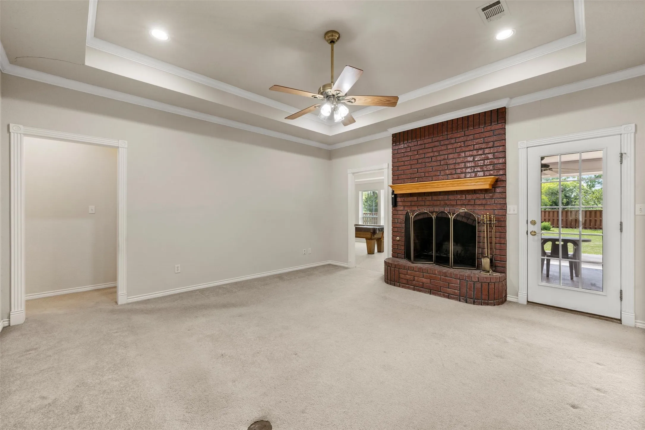 Brick fireplace with a wood-finish mantelpiece, ceiling fan, and recessed lighting