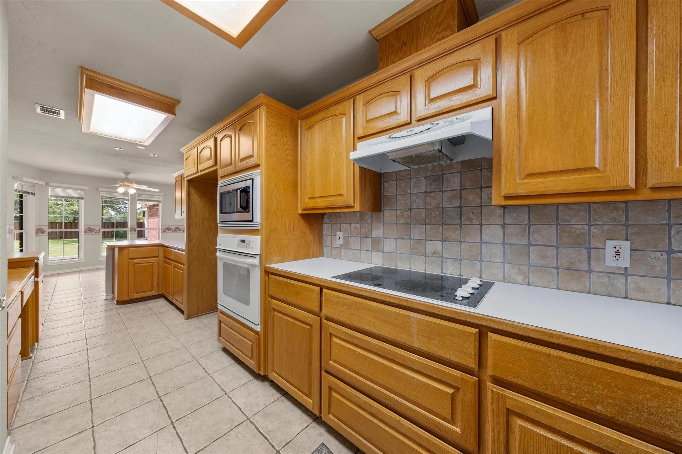Kitchen featuring light wood cabinetry, white countertops, tile flooring, and a tile backsplash