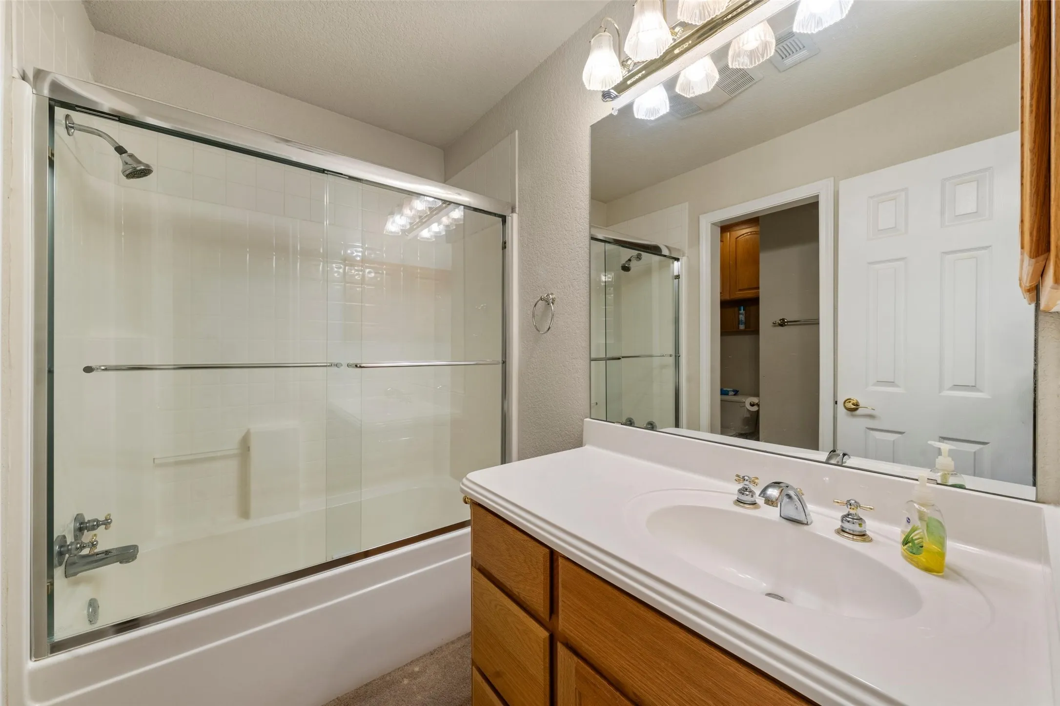 Bathroom featuring a bathtub with a sliding glass enclosure, an integrated shower, and a single vanity with a white countertop and wood-finish cabinetry
