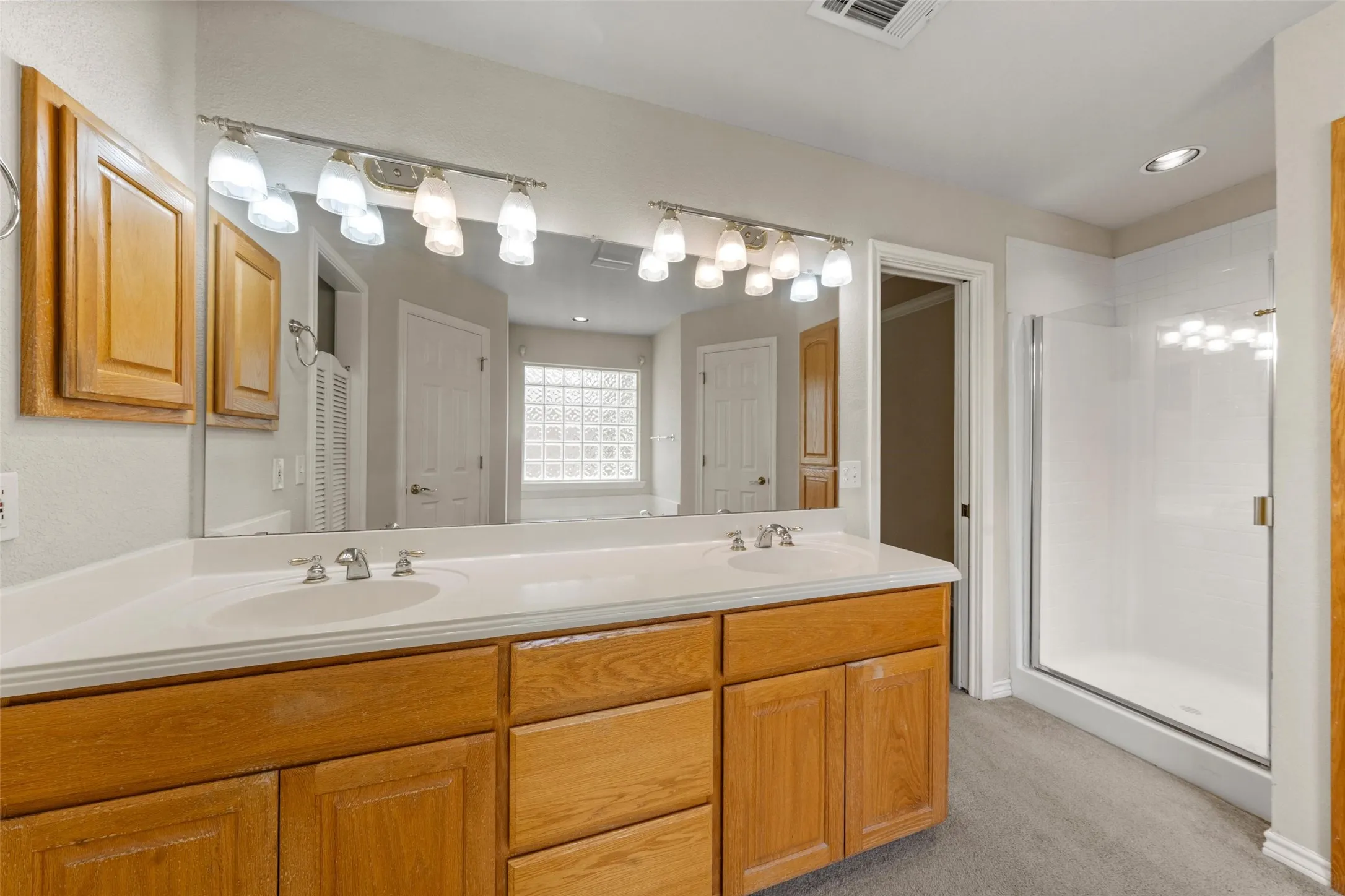 Bathroom vanity with dual sinks, a large mirror, and overhead lighting