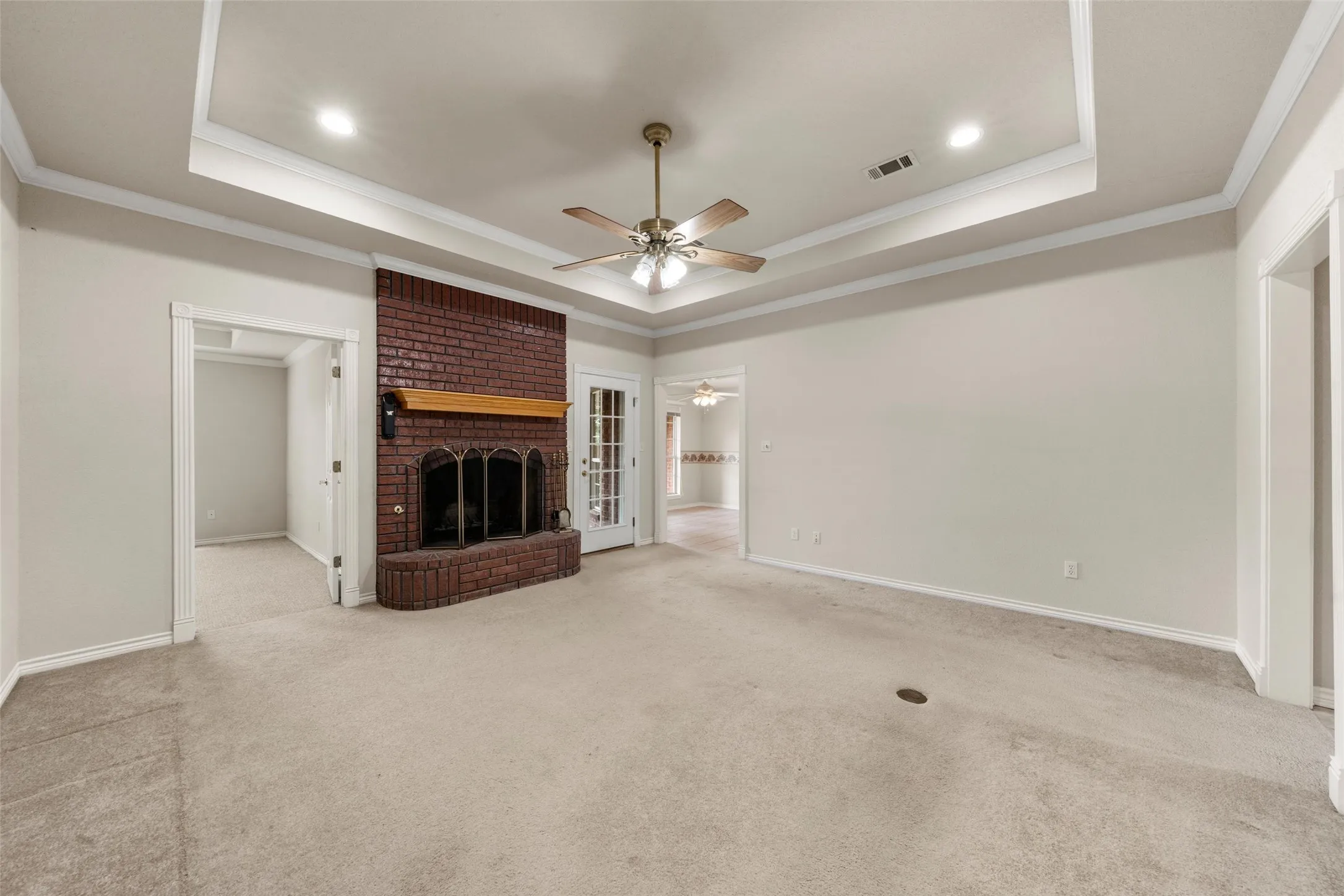 Red brick fireplace with a wood mantel, recessed lighting, ceiling fan, carpet flooring, and tray ceiling with crown molding