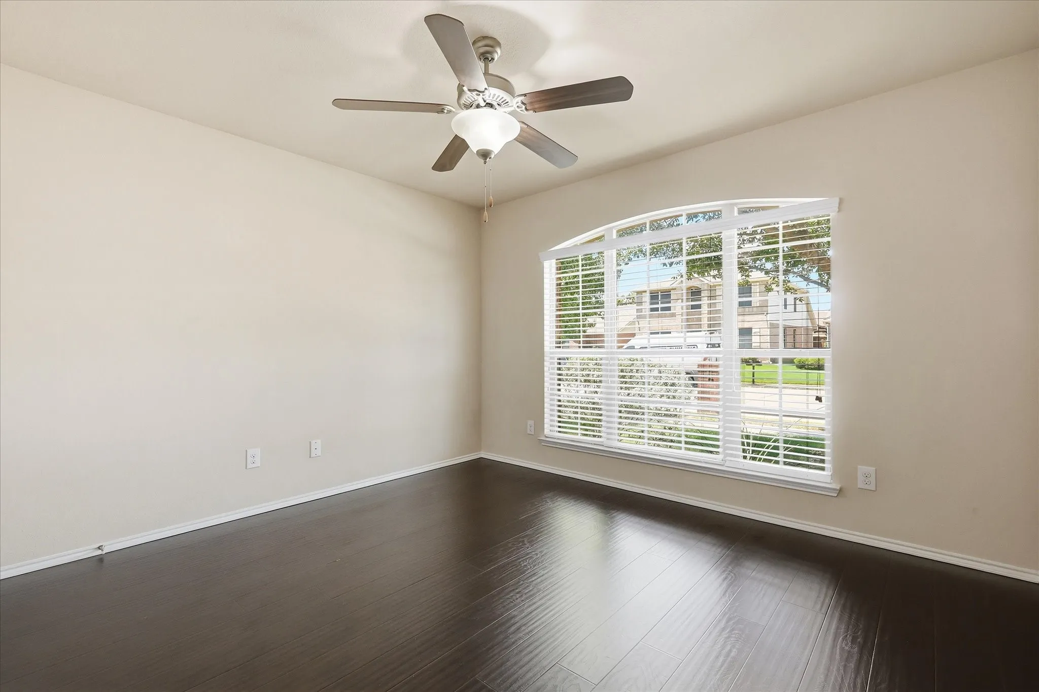Room featuring wood-finish flooring, neutral wall tones, and an arched window with horizontal blinds