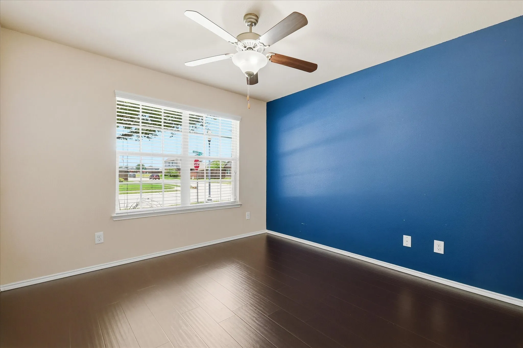 Spacious room featuring wood-finish flooring, a prominent accent wall, and a large window with white blinds