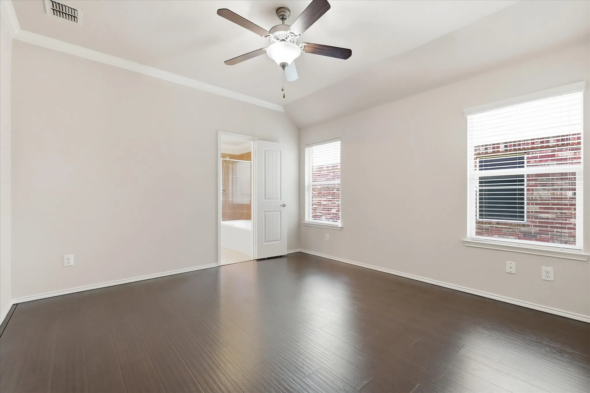 Spacious room featuring vaulted ceilings, dark wood-finish flooring, two windows with blinds, crown molding, and a ceiling fan with integrated lighting