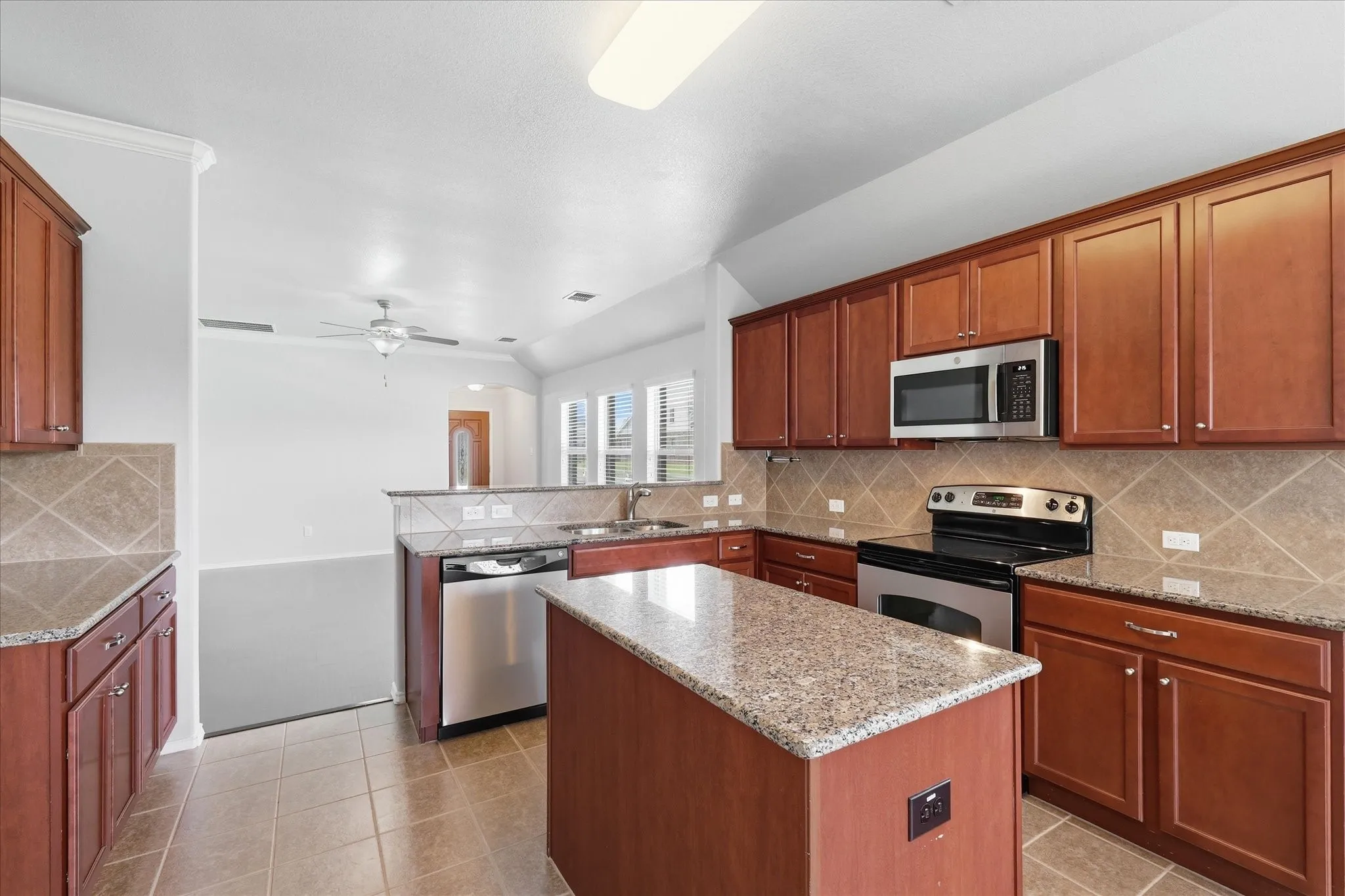 Kitchen featuring an island, tile flooring, granite countertops, cherry wood-finish cabinetry, and stainless steel appliances