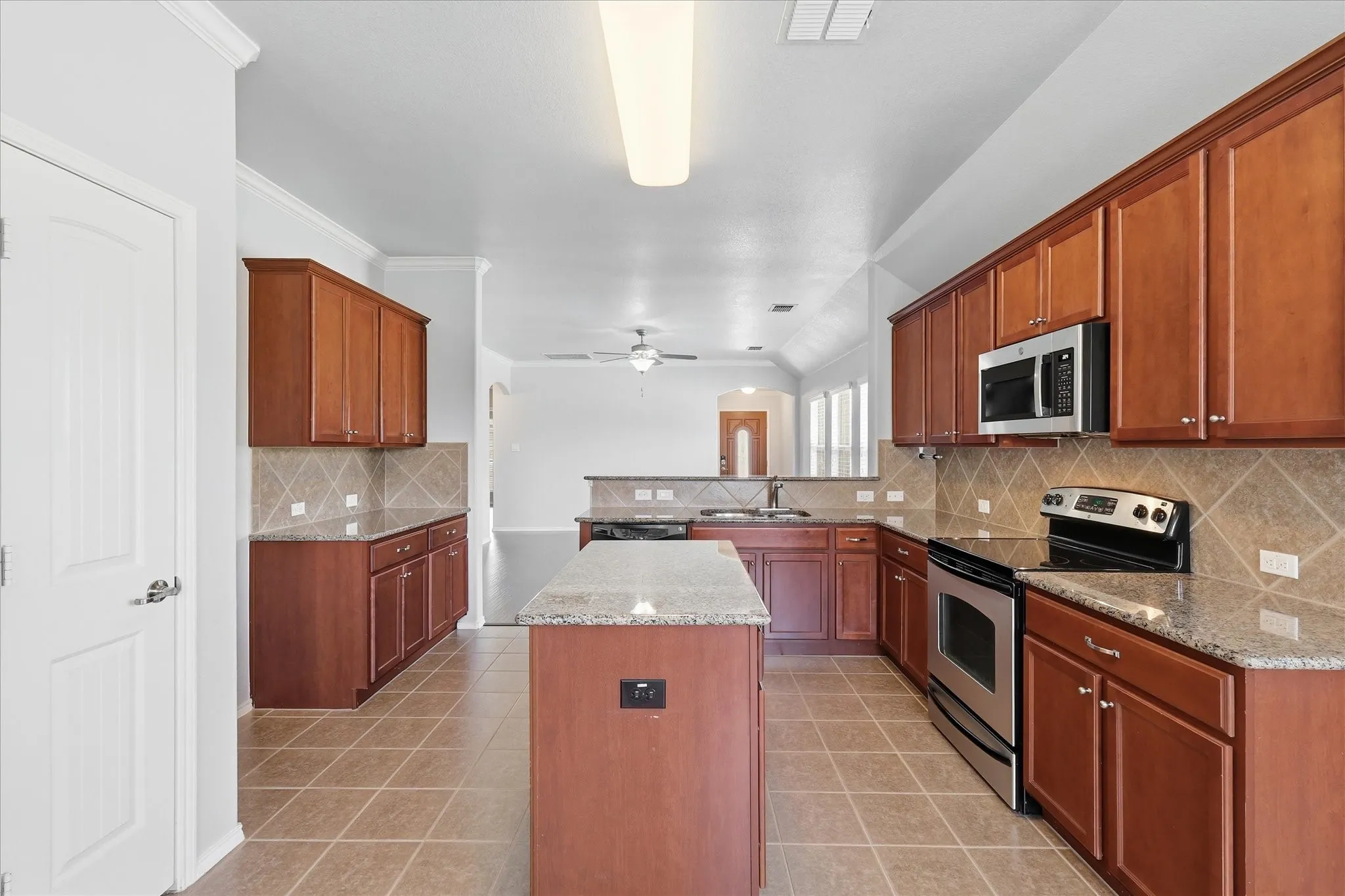 Open-concept kitchen featuring wood cabinetry, granite countertops, stainless steel appliances, a tiled backsplash, and an island with a breakfast bar