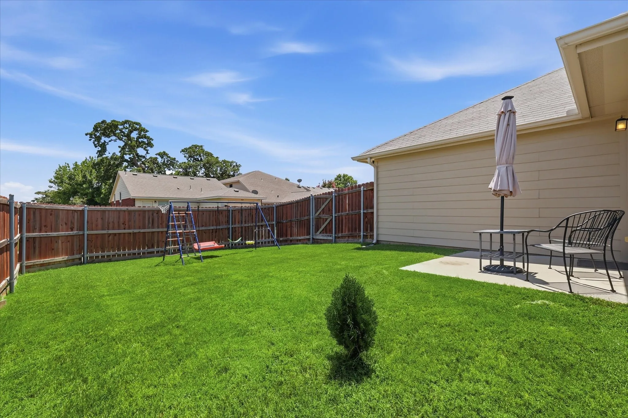 Expansive backyard featuring a manicured lawn, full privacy fencing, and a concrete patio