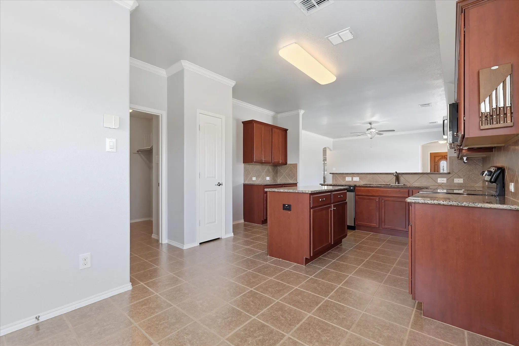 Kitchen featuring tile flooring, wood cabinetry, stone countertops, and a central island with storage