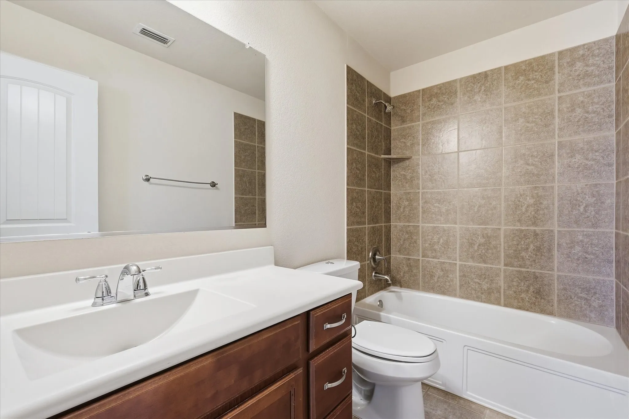 Bathroom featuring a wood-finish vanity with a white countertop and integrated sink, chrome faucet, and a large wall-mounted mirror