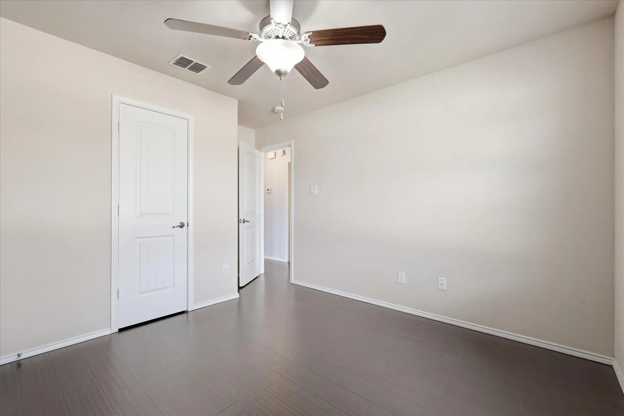 Spacious interior room featuring dark wood-finish flooring and neutral wall tones