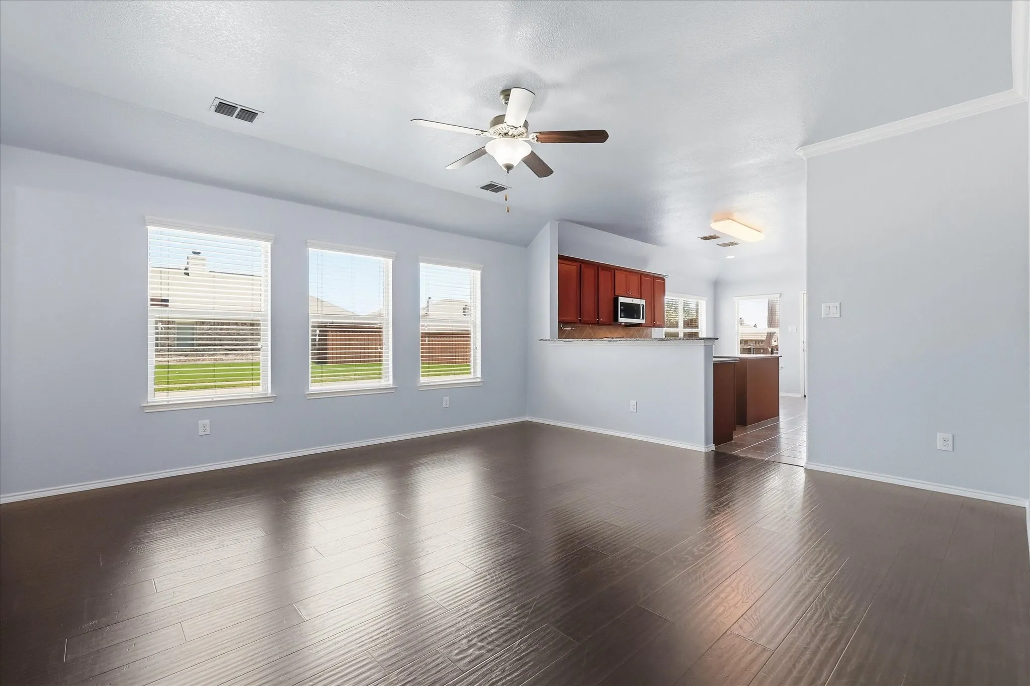 Open concept living area featuring dark wood-finish flooring, a ceiling fan, and multiple windows with horizontal blinds