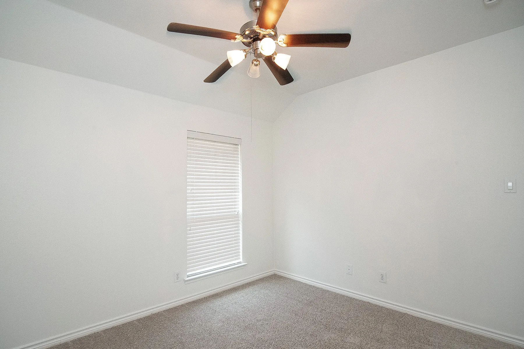 Vaulted ceiling featuring a ceiling fan with integrated lighting, window with blinds, and neutral-toned carpet flooring
