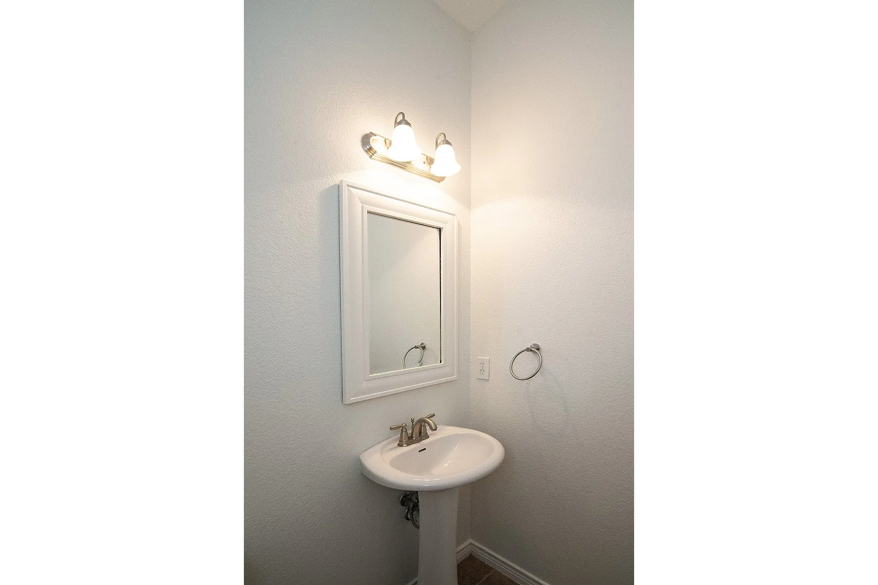 Pedestal sink with white basin, framed mirror, and chrome-finish light fixture