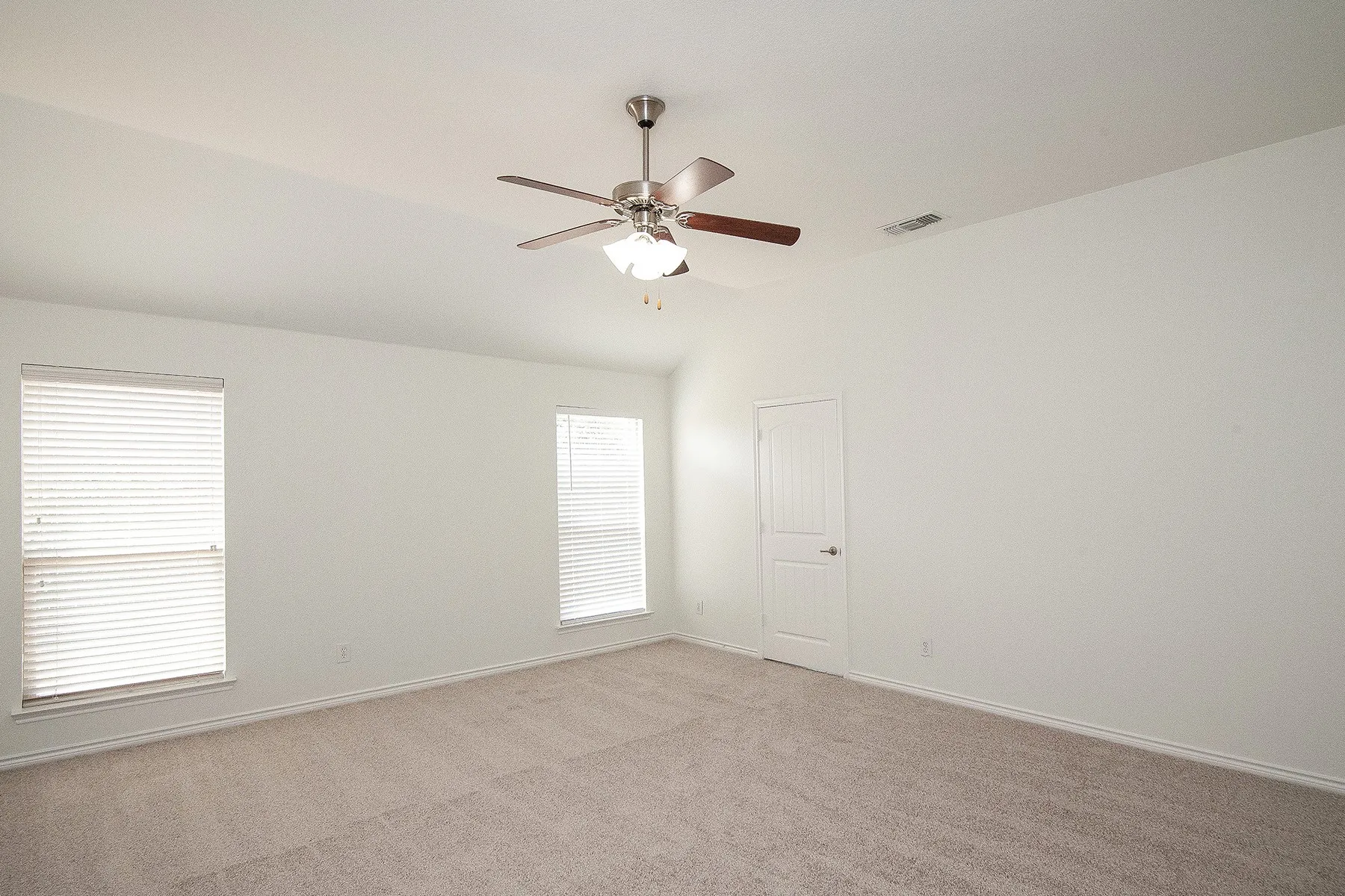 Vaulted ceiling with an integrated ceiling fan and light fixture, two windows with blinds, plush carpet flooring, and a white paneled door