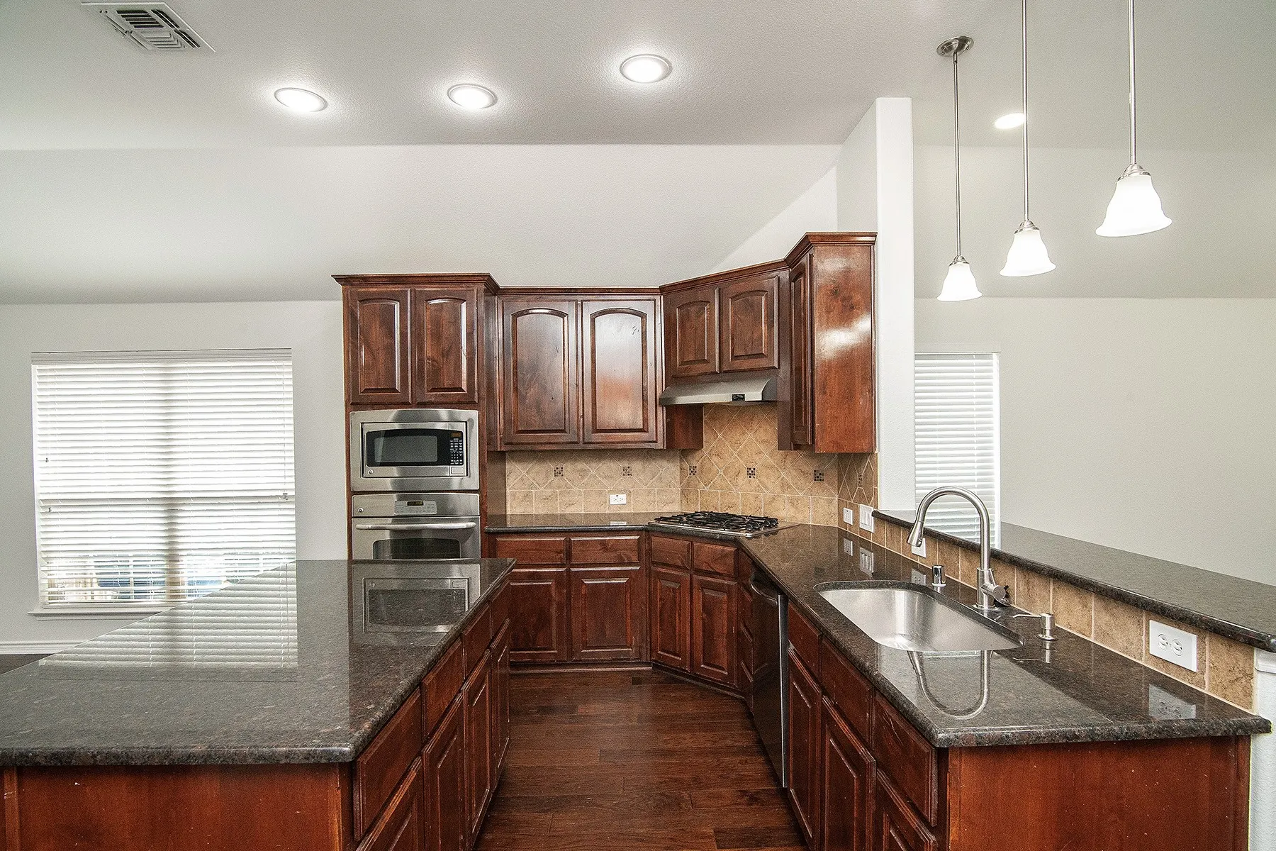 Kitchen featuring dark wood cabinetry, stainless steel appliances, granite countertops, and a tile backsplash