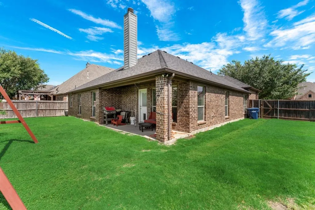 Expansive green lawn surrounds a brick exterior featuring multiple windows and a covered patio