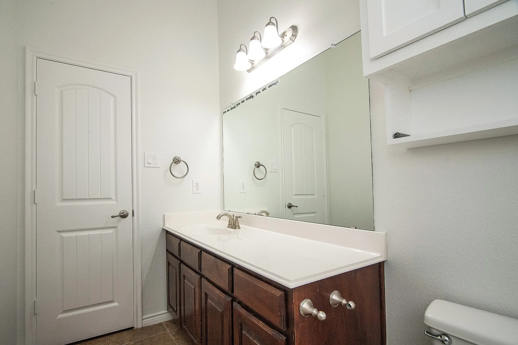 Elegant bathroom vanity featuring rich wood cabinetry with multiple drawers and chrome hardware, paired with a spacious white countertop and brushed nickel faucet