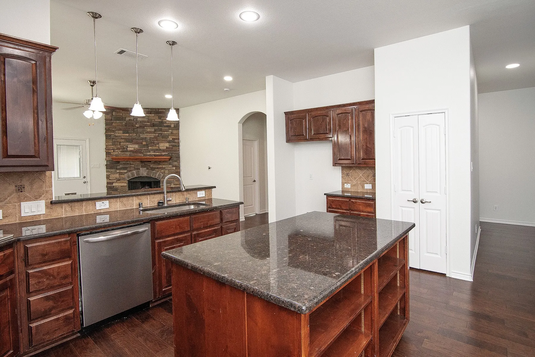 Kitchen featuring wood-finish flooring, dark wood cabinetry, a center island with countertop, stainless steel dishwasher, and recessed lighting