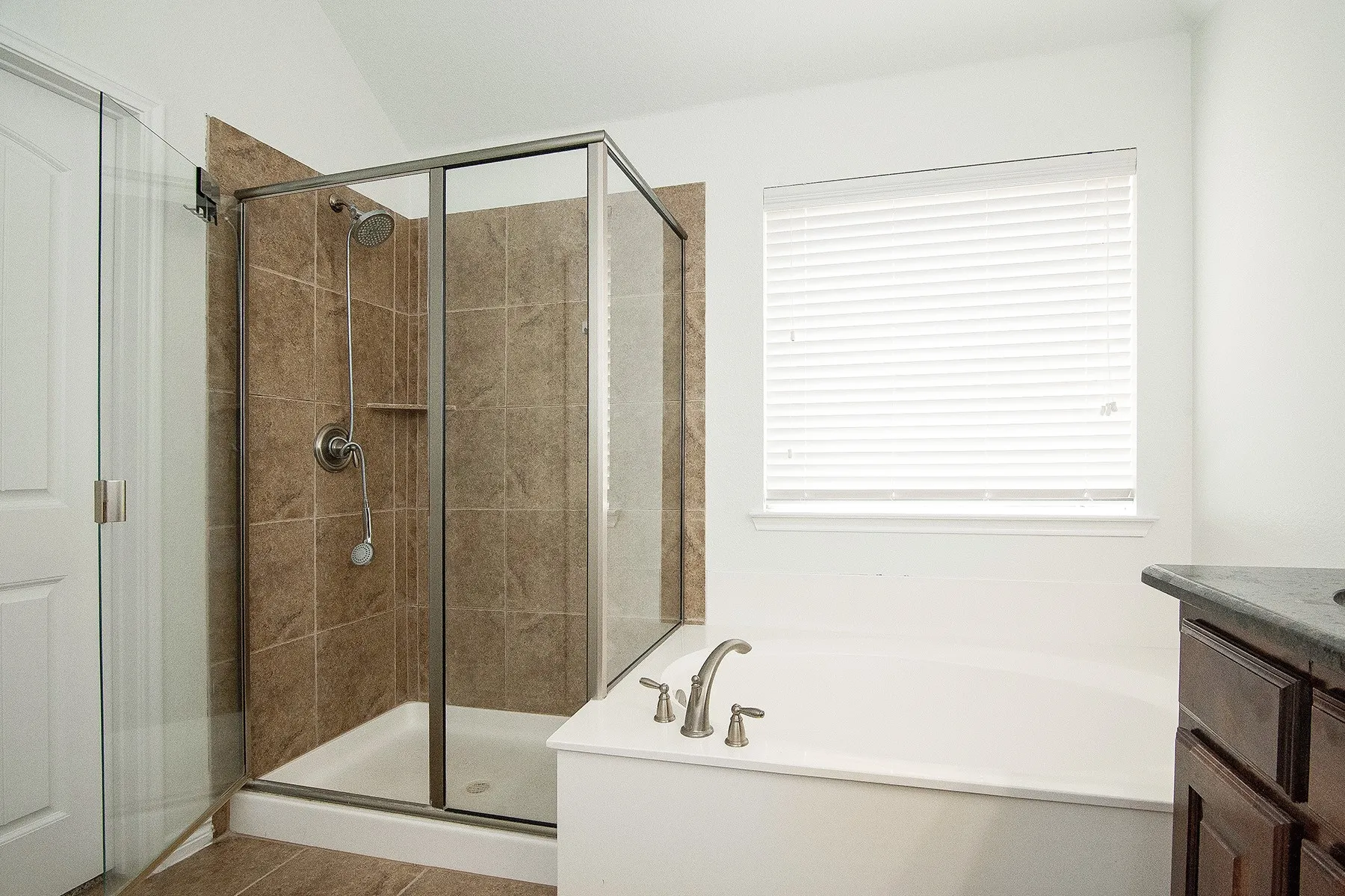 Tiled walk-in shower with a glass enclosure, separate soaking tub with deck-mounted fixtures, and a vanity with a dark countertop