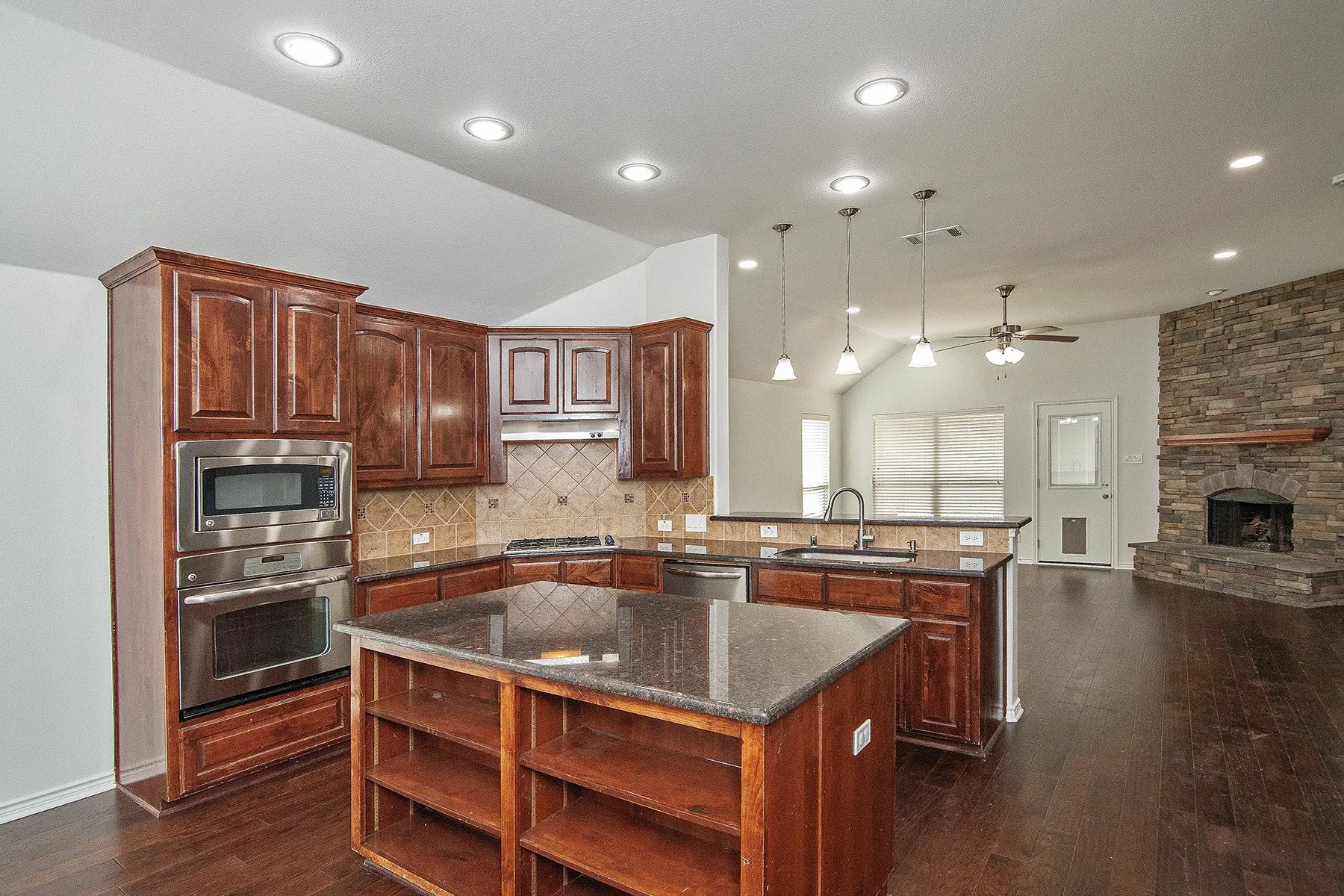 Chef's kitchen featuring rich wood cabinetry, stainless steel appliances including double wall ovens, granite countertops, and a large center island with open shelving