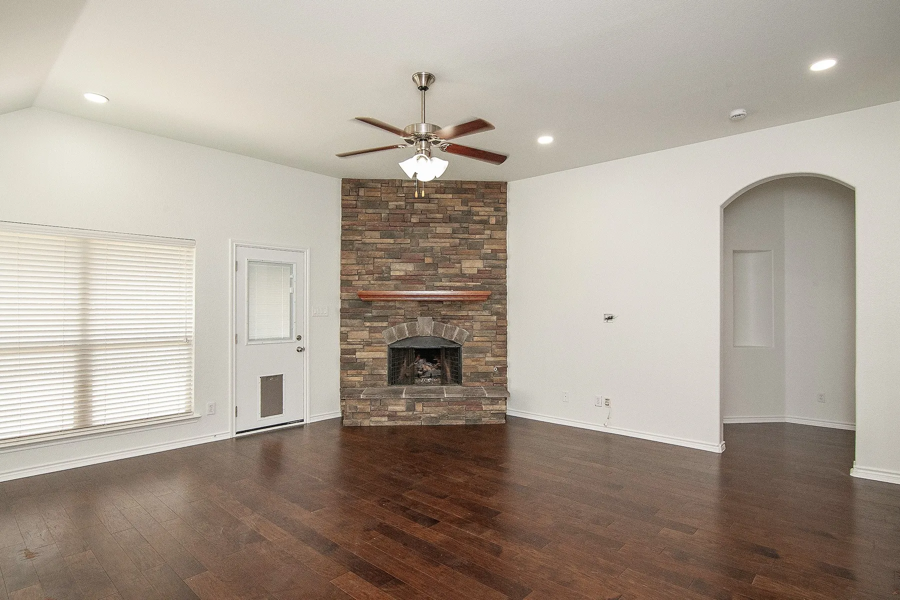 Vaulted ceiling, wood-finish flooring, stone-clad fireplace with wood mantel, ceiling fan with integrated lighting, and recessed lighting