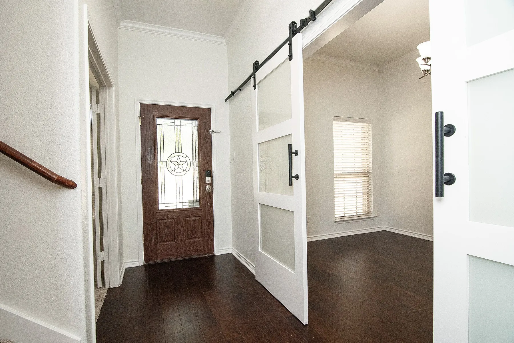 Welcoming foyer showcasing dark wood-finish flooring, white shaker-style interior doors with matte black hardware, decorative glass-panel entry door with sidelights, and bright natural light from multiple windows
