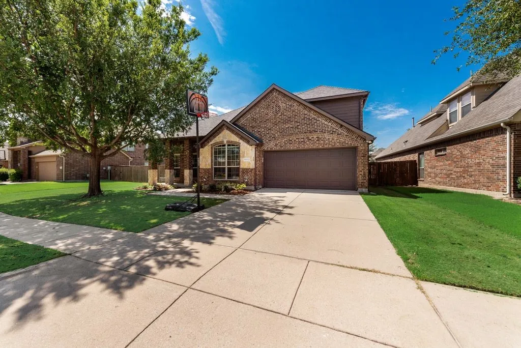 Brick and stone facade residence featuring an attached two-car garage, mature front yard tree, and an expansive concrete driveway