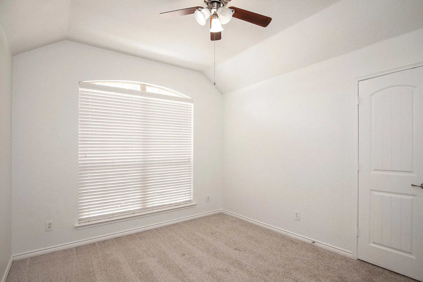 Vaulted ceiling, arched window, ceiling fan with light fixture, carpeted flooring, and paneled door with hardware