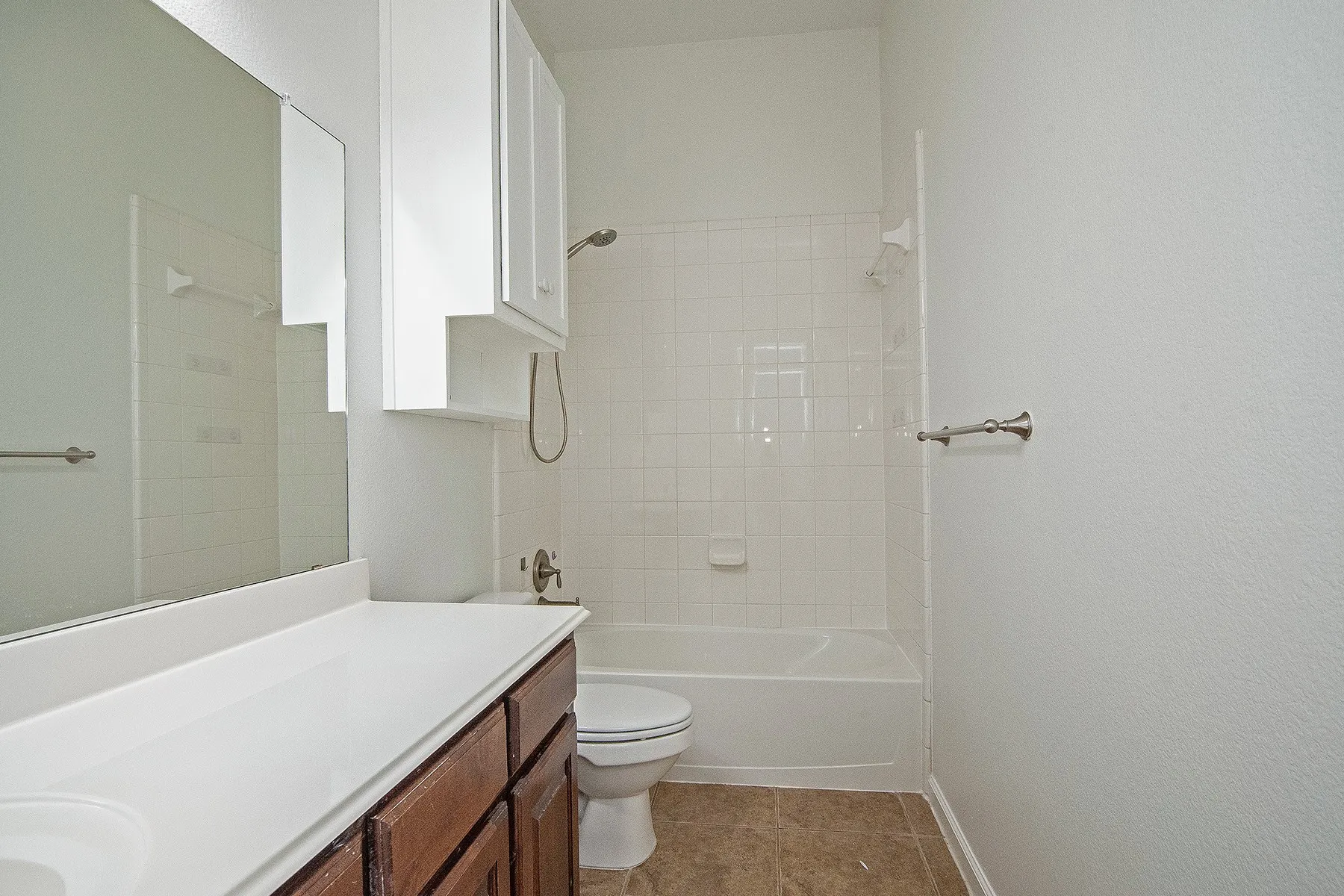White subway tile shower surround, built-in bathtub, white vanity countertop, wood-finish cabinetry, and built-in mirror