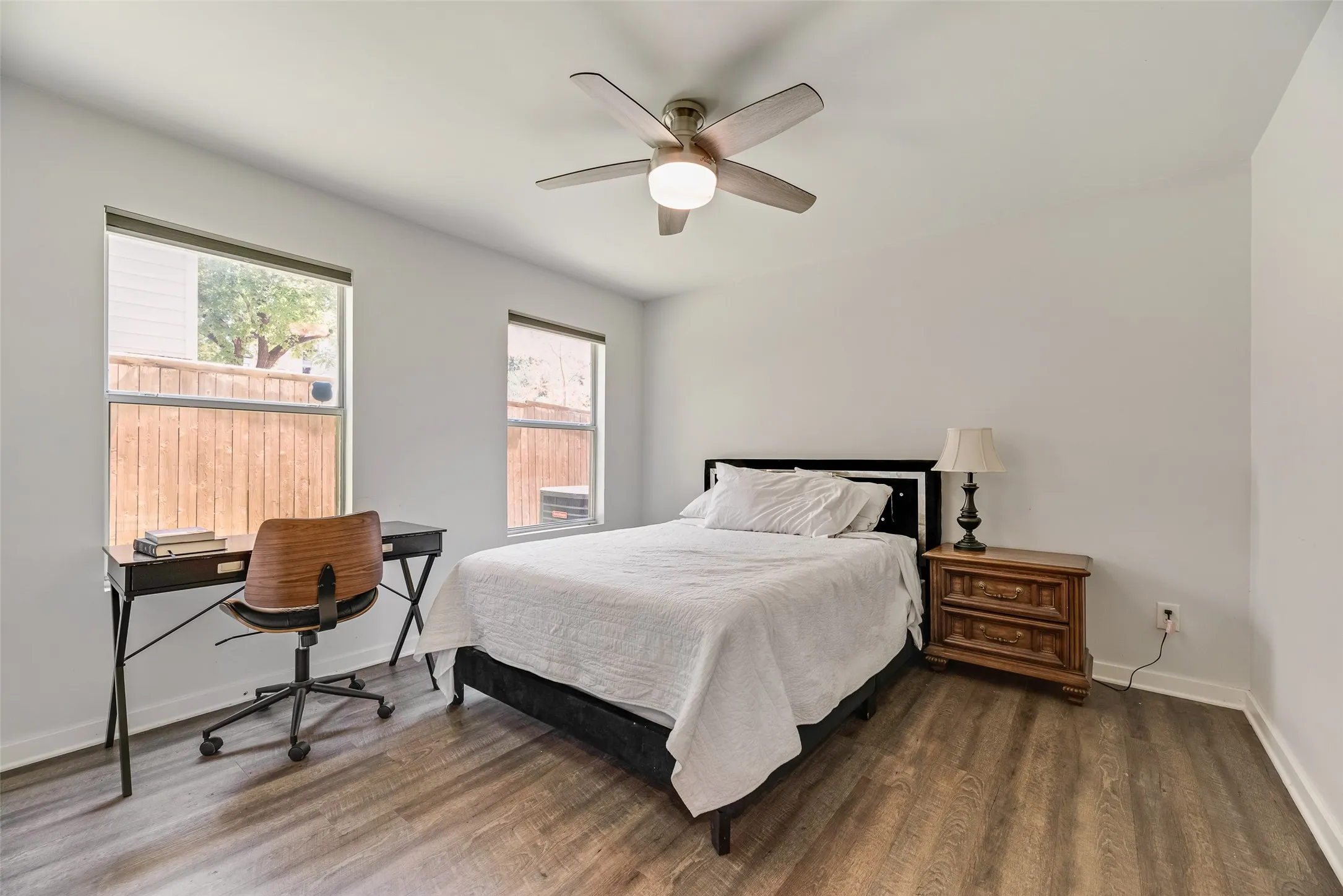 Bedroom featuring wood-finish flooring, two windows, a ceiling fan with integrated lighting, and neutral wall tones