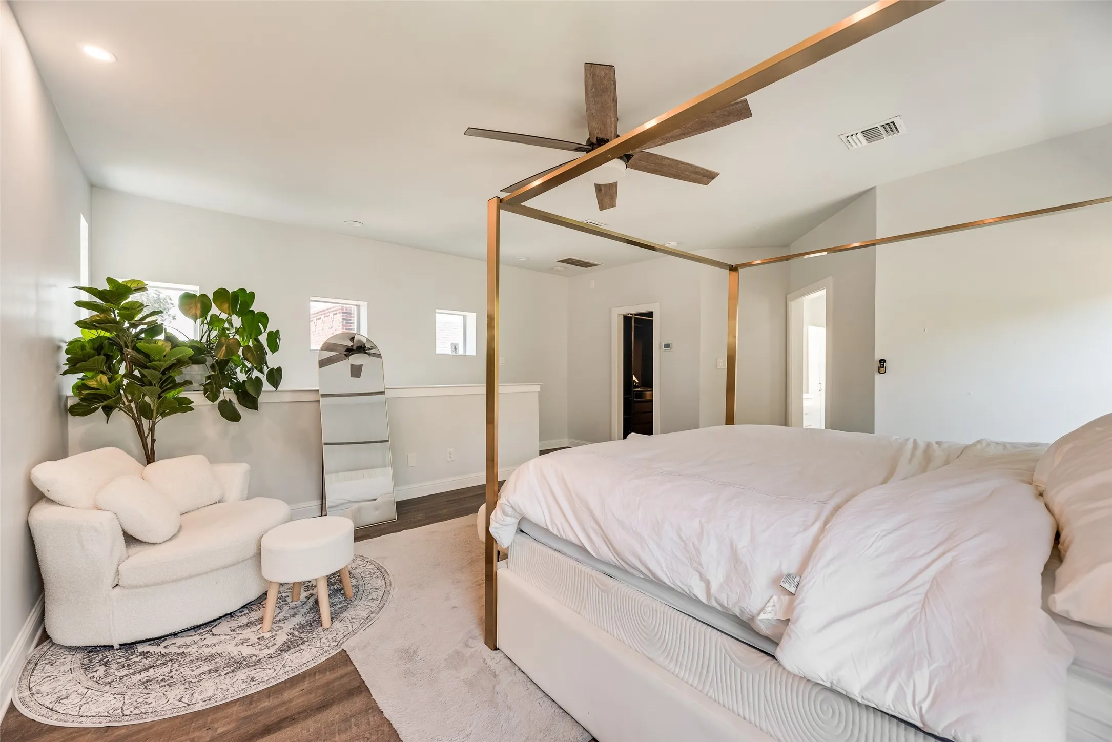 Spacious bedroom featuring vaulted ceilings, wood-finish flooring, a contemporary ceiling fan, recessed lighting, and multiple windows for natural illumination