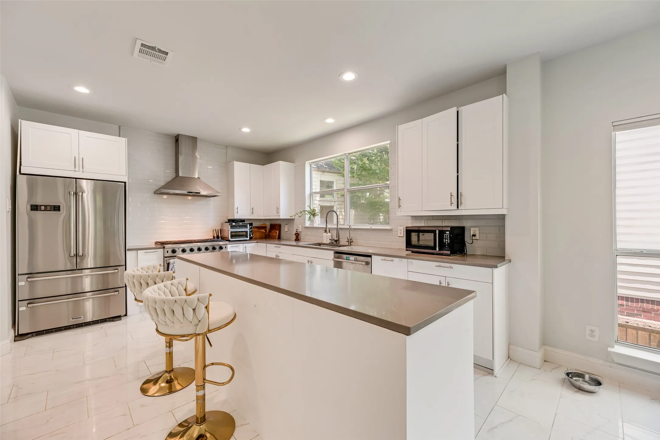 Modern kitchen featuring stainless steel appliances, white cabinetry with dark hardware, a center island with a solid surface countertop, white subway tile backsplash, and recessed lighting
