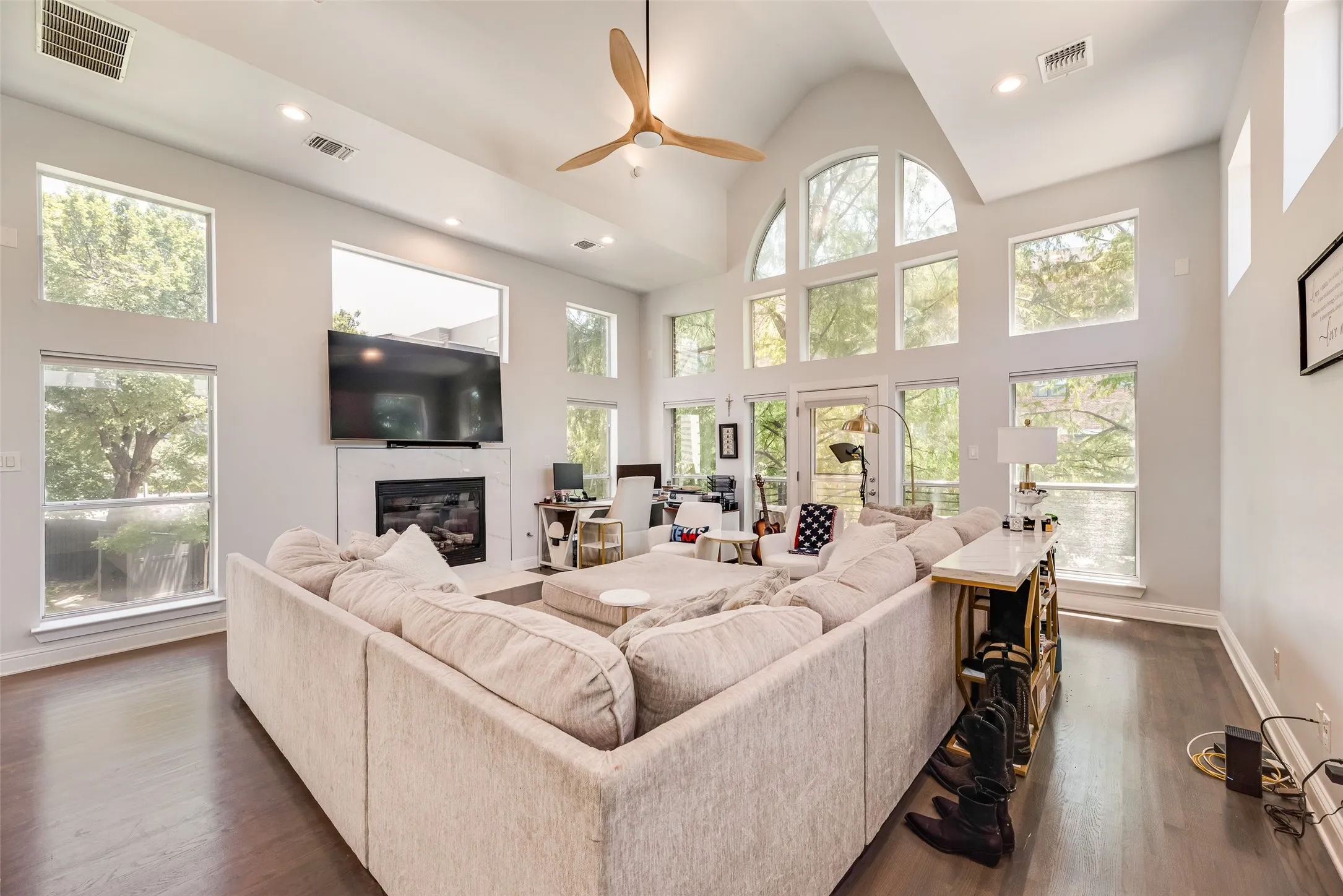 Vaulted ceilings with a wood-finish ceiling fan, wood-finish flooring, a white mantel fireplace, abundant multi-pane windows, and recessed lighting