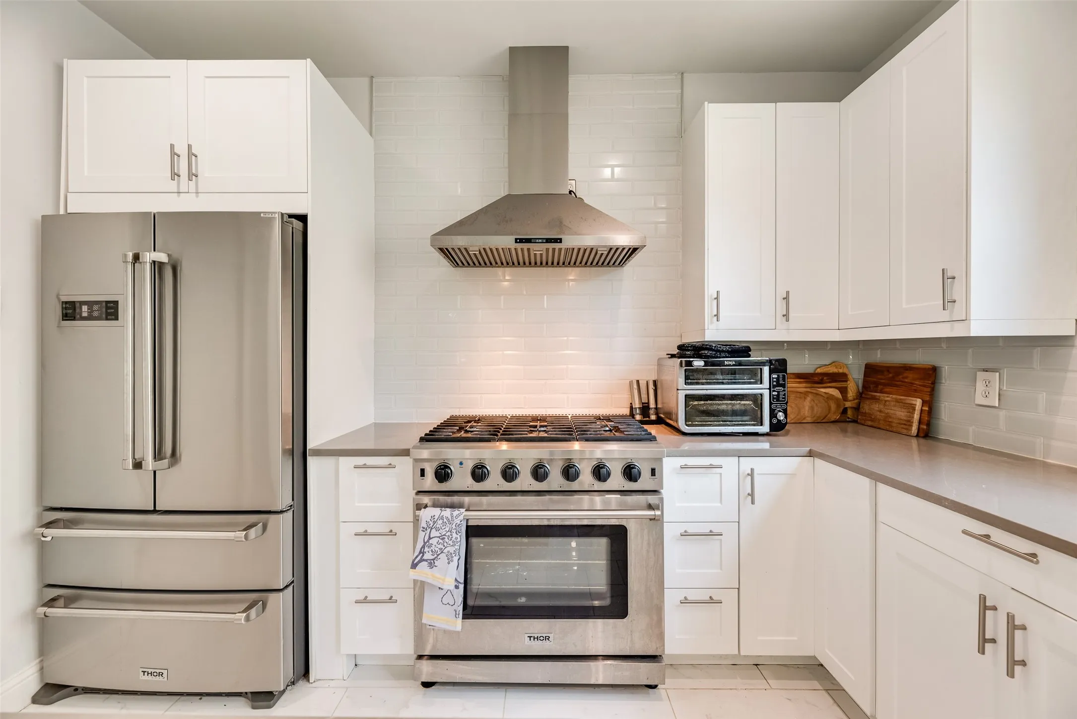 Modern kitchen featuring white shaker cabinetry, stainless steel appliances, a professional-grade range with a coordinating hood, grey countertops, and a white subway tile backsplash