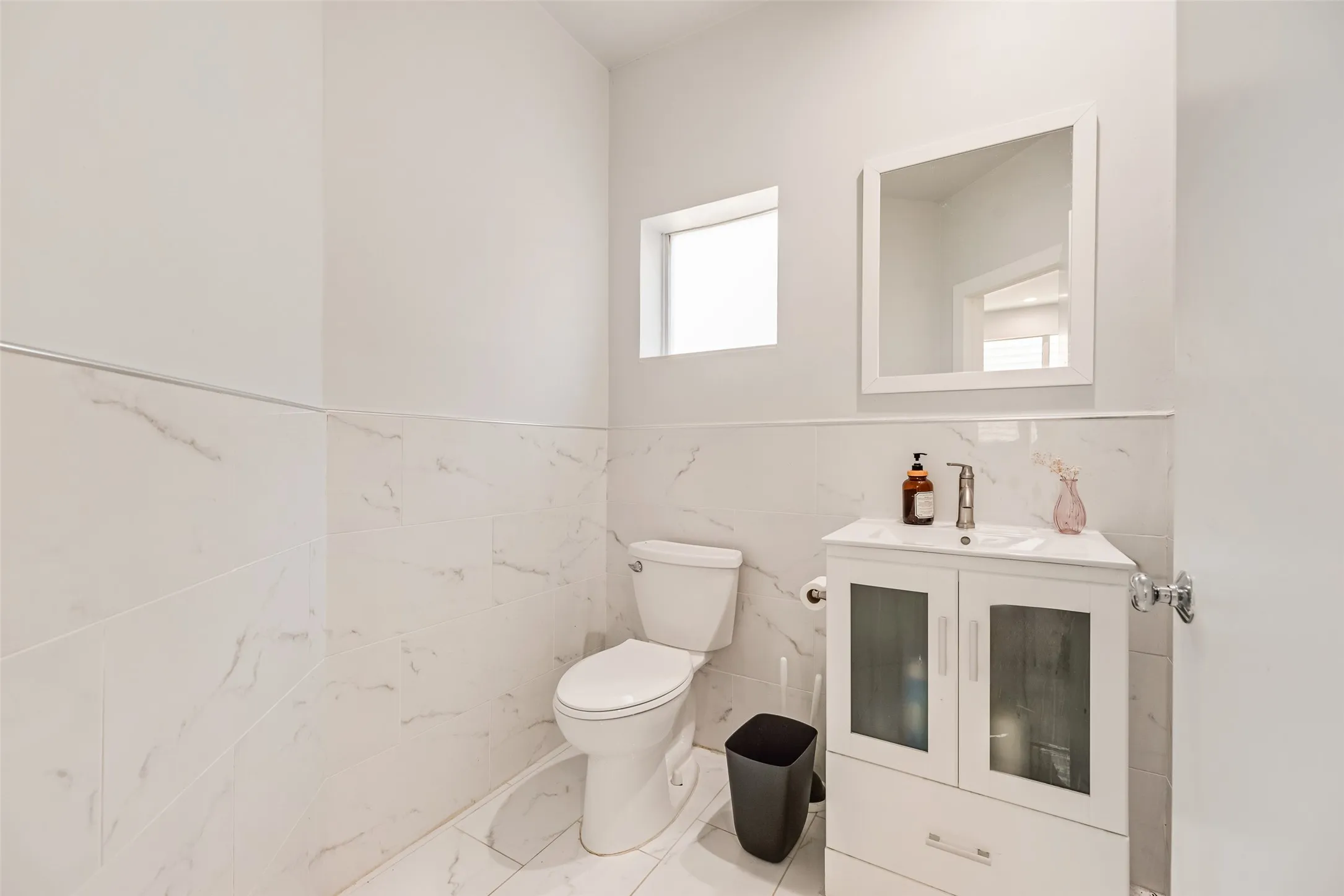 Bathroom featuring a white vanity with integrated sink, square mirror, and white marble-look tile flooring