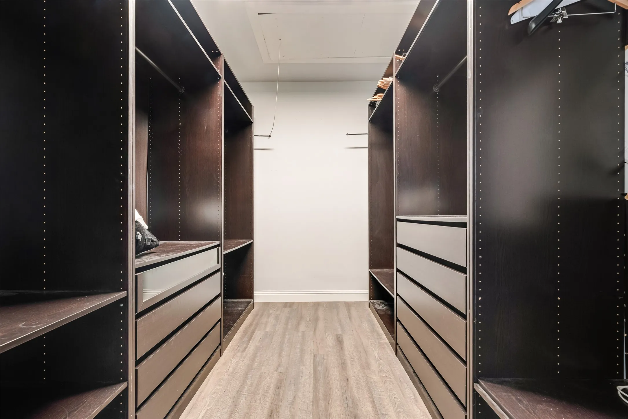 Custom closet system featuring dark wood-finish cabinetry, extensive shelving, integrated drawers, hanging rods, and light wood-finish flooring