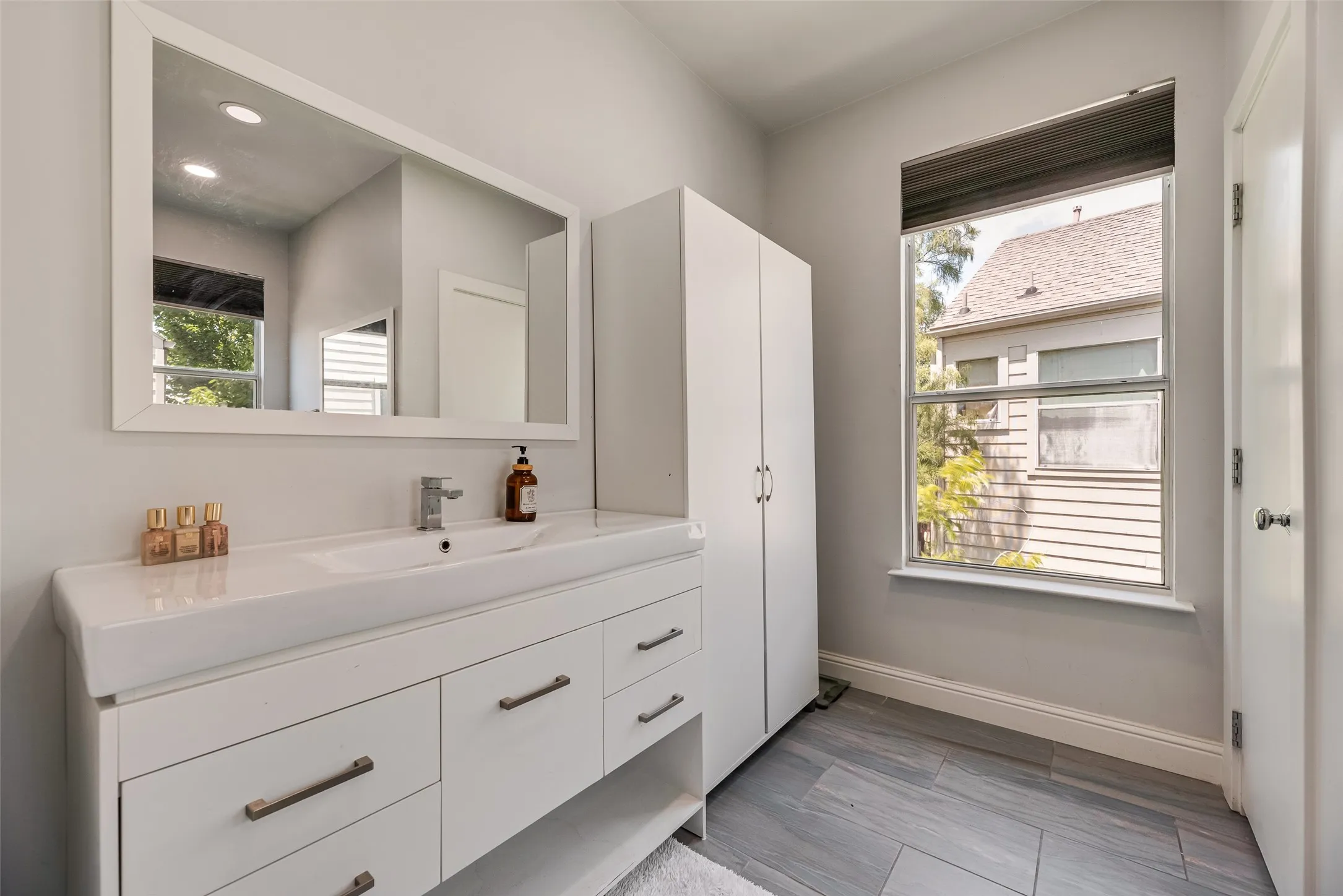Contemporary bathroom featuring a white vanity with integrated sink, rectangular framed mirror, and a white storage cabinet