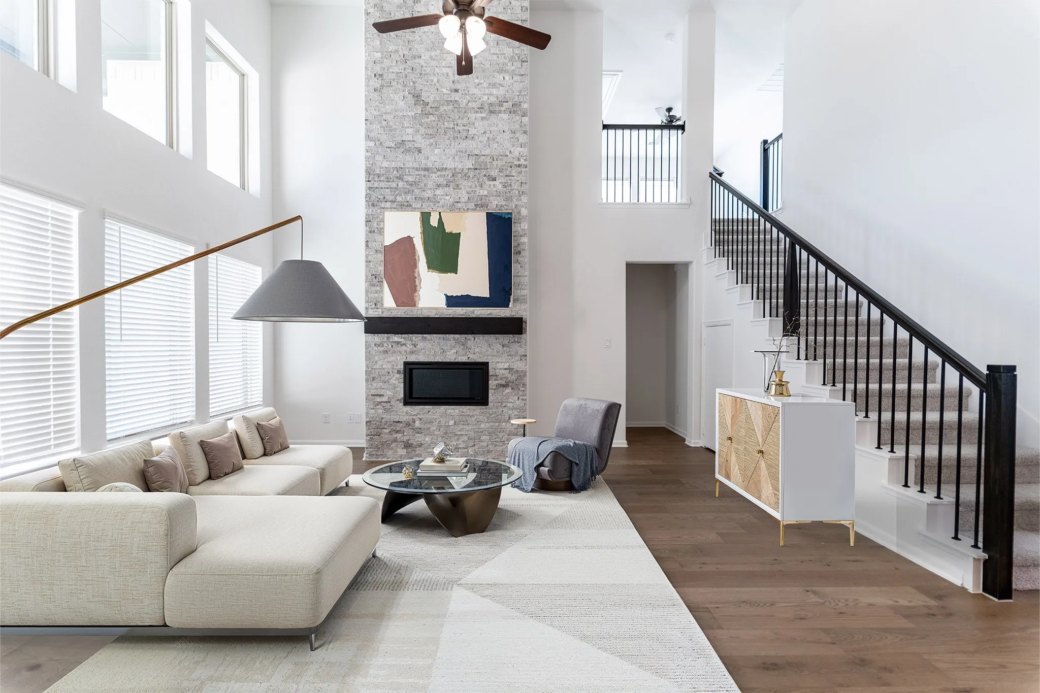 Two-story living area featuring a stone fireplace, wood-finish flooring, and a staircase with wrought iron balusters