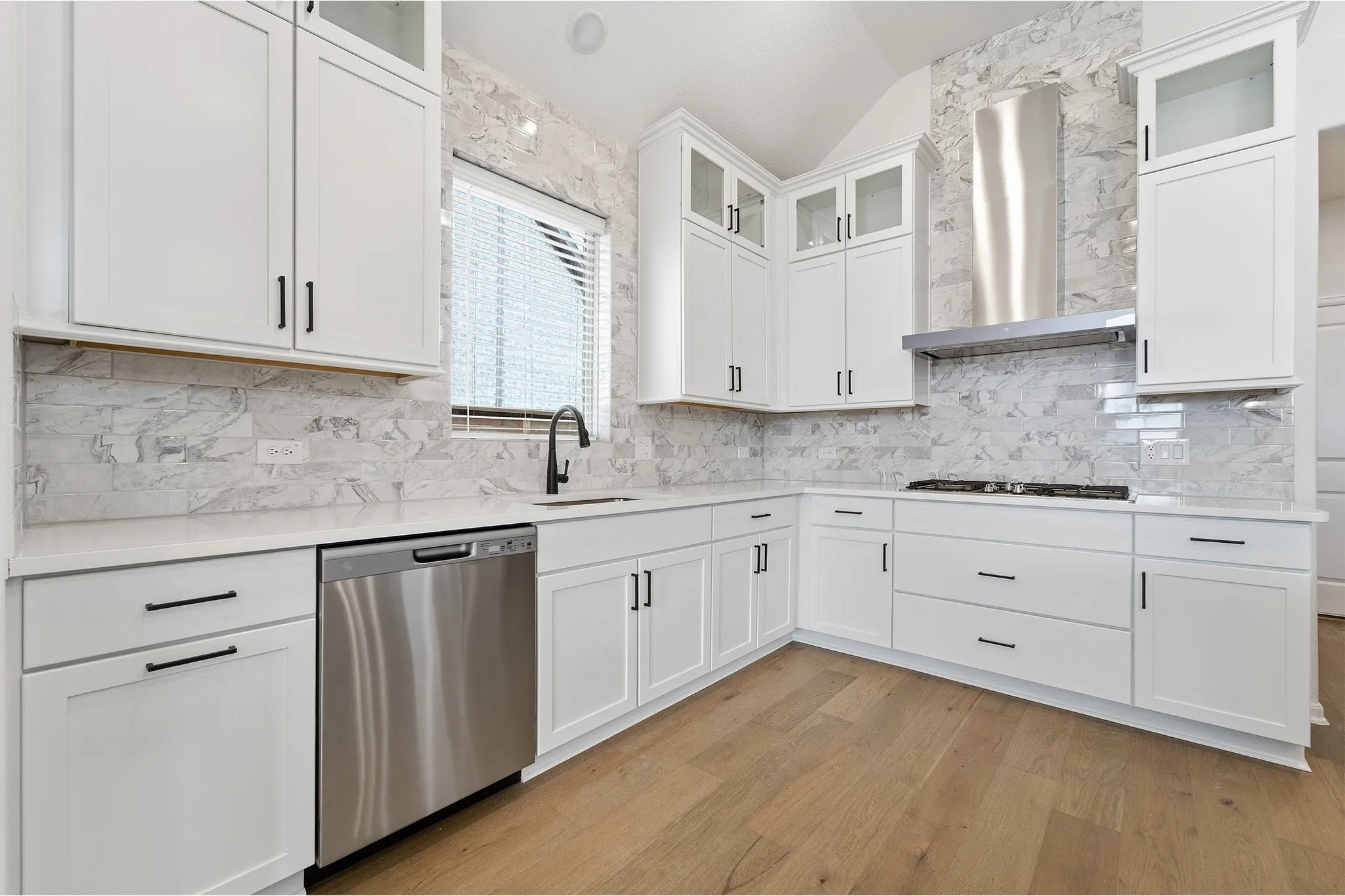 Modern kitchen featuring white shaker cabinetry, stainless steel appliances, marble-look subway tile backsplash, quartz countertops, and wood-finish flooring