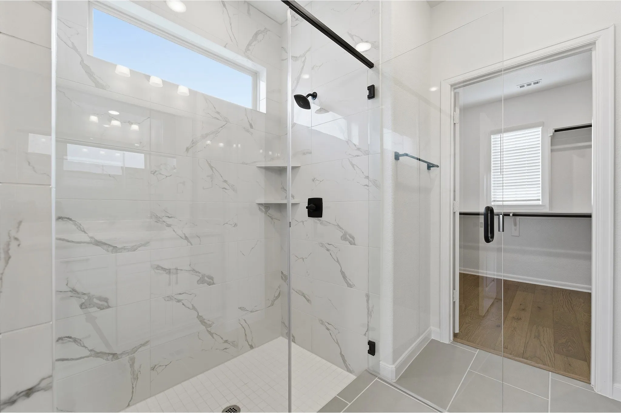 Expansive walk-in shower featuring a frameless glass enclosure, white and gray veined tile, integrated corner shelving, and matte black fixtures