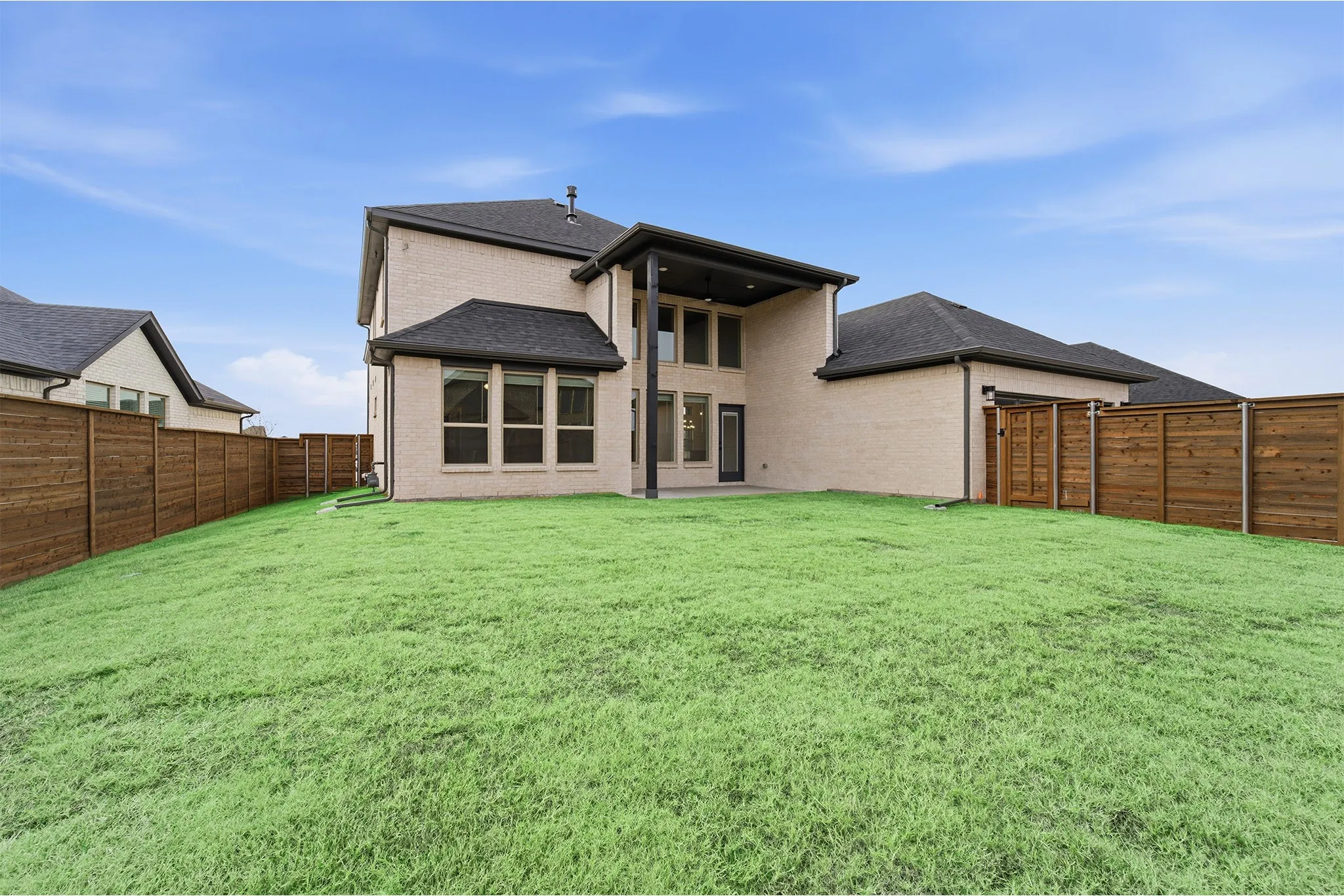 Expansive rear lawn featuring a privacy fence and a two-story brick exterior